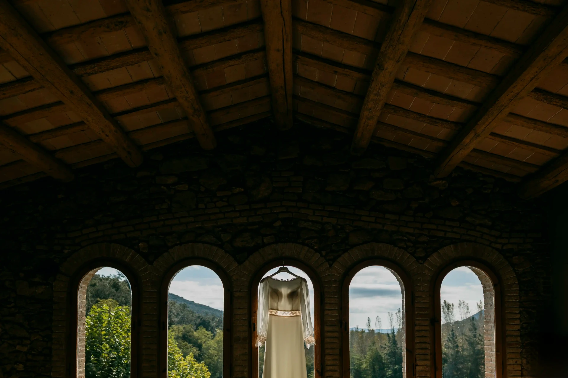 Vestido de novia colgado en el arco de una ventana con vistas al Montseny en Can Riera de la Pineda