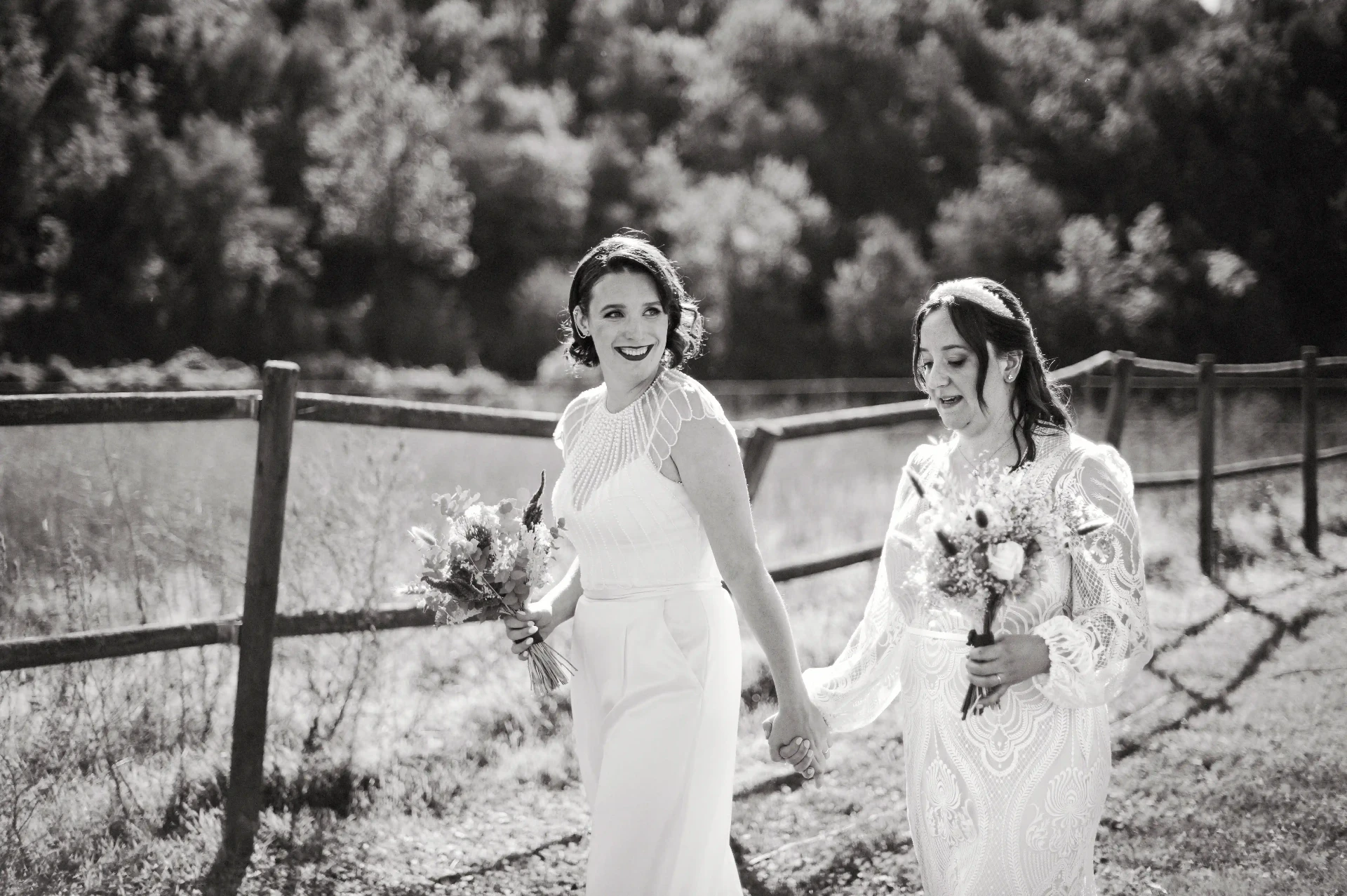 Retrato en blanco y negro de las dos novias caminando de la mano junto a la valla de madera en This Must Be The Place