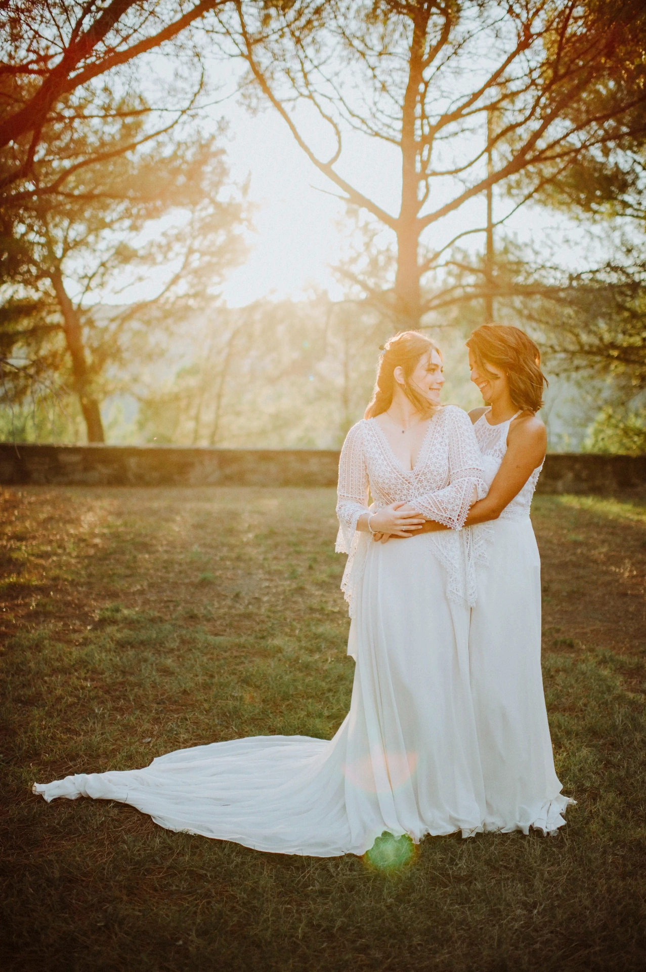 boda LGTBI en Ca n'Alzina (Rubió) — retrato de pareja de las novias abrazadas bajo los pinos con contraluz dorado