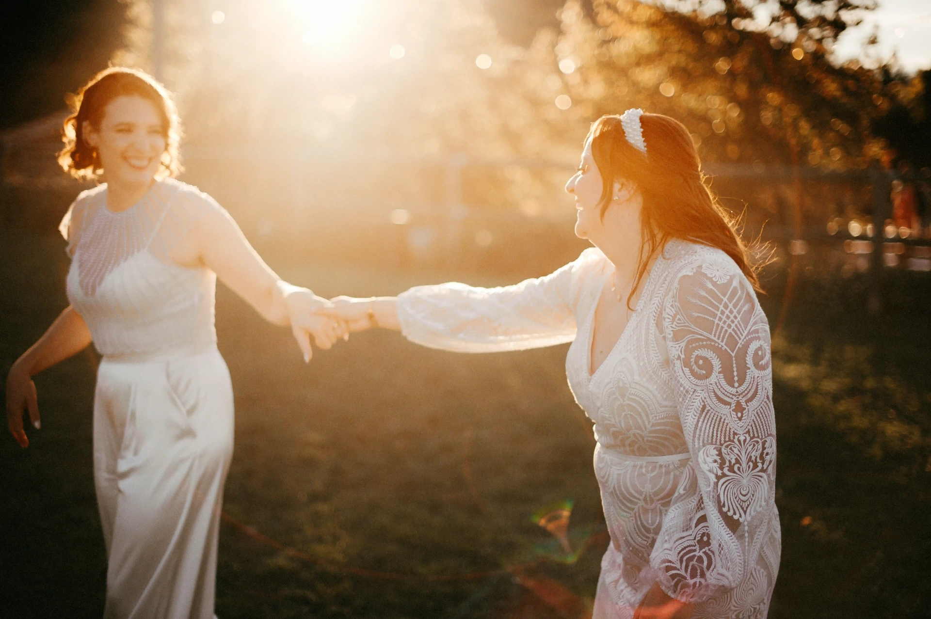 Las dos novias bailando de la mano bajo el contraluz dorado del atardecer en el prado de This Must Be The Place