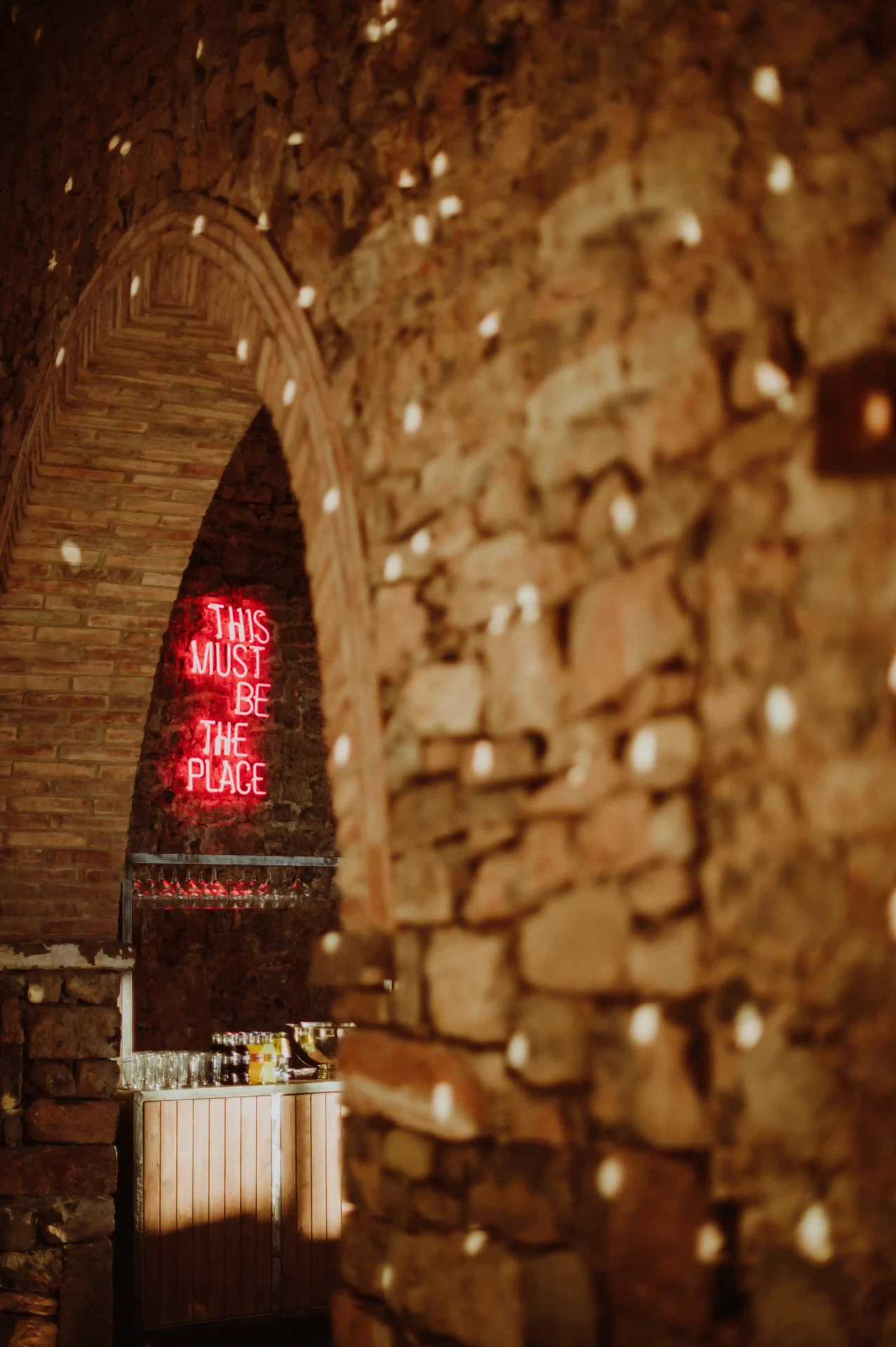 Detalle del neón 'This Must Be The Place' iluminando el bar de piedra de la masía en el Moianès