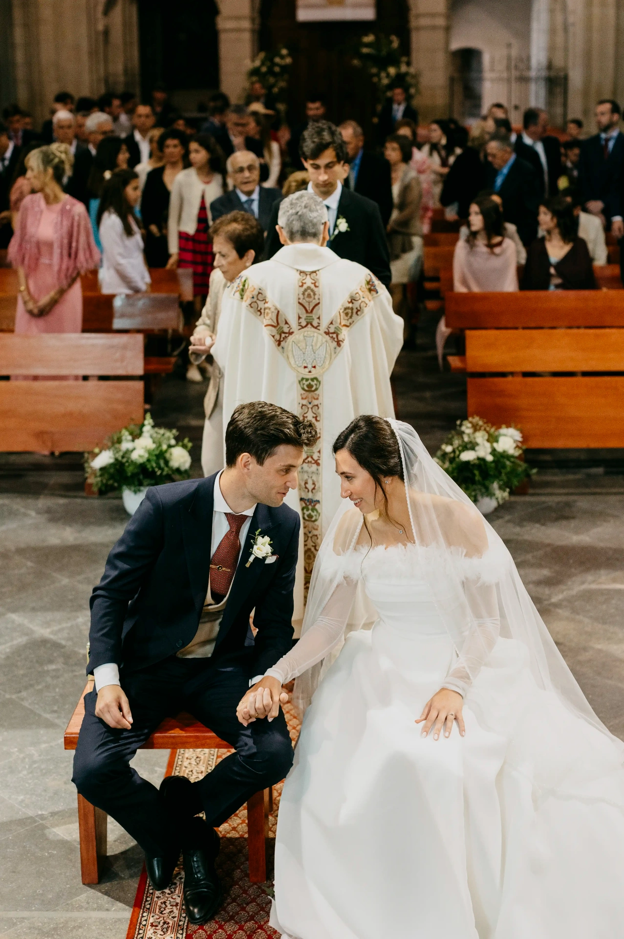 Novios cogidos de la mano sentados durante la homilía mientras el sacerdote se dirige a los invitados, boda en Cervera (Lleida)