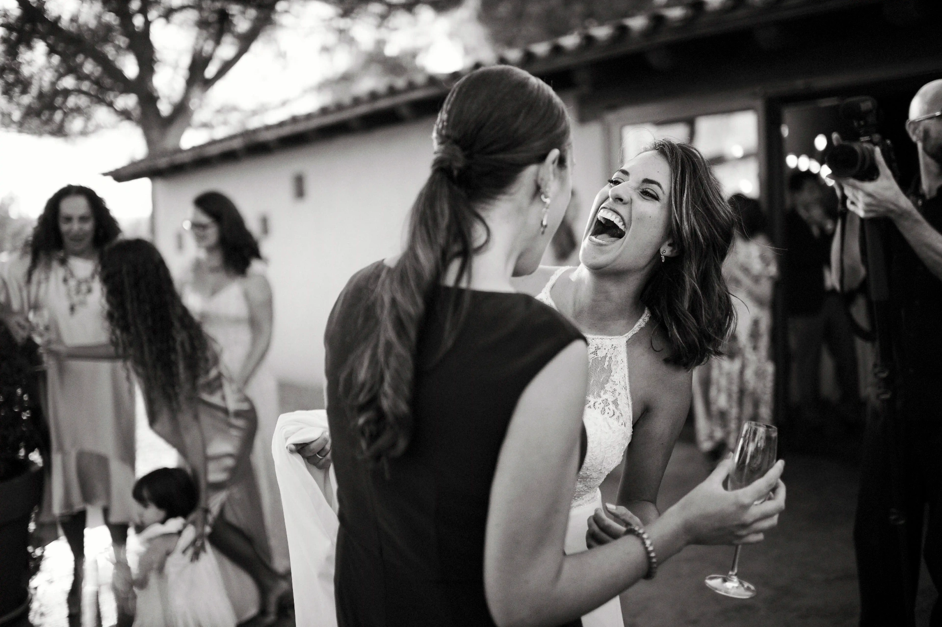 boda LGTBI en Ca n'Alzina — novia riendo a carcajadas con una invitada durante el aperitivo en blanco y negro