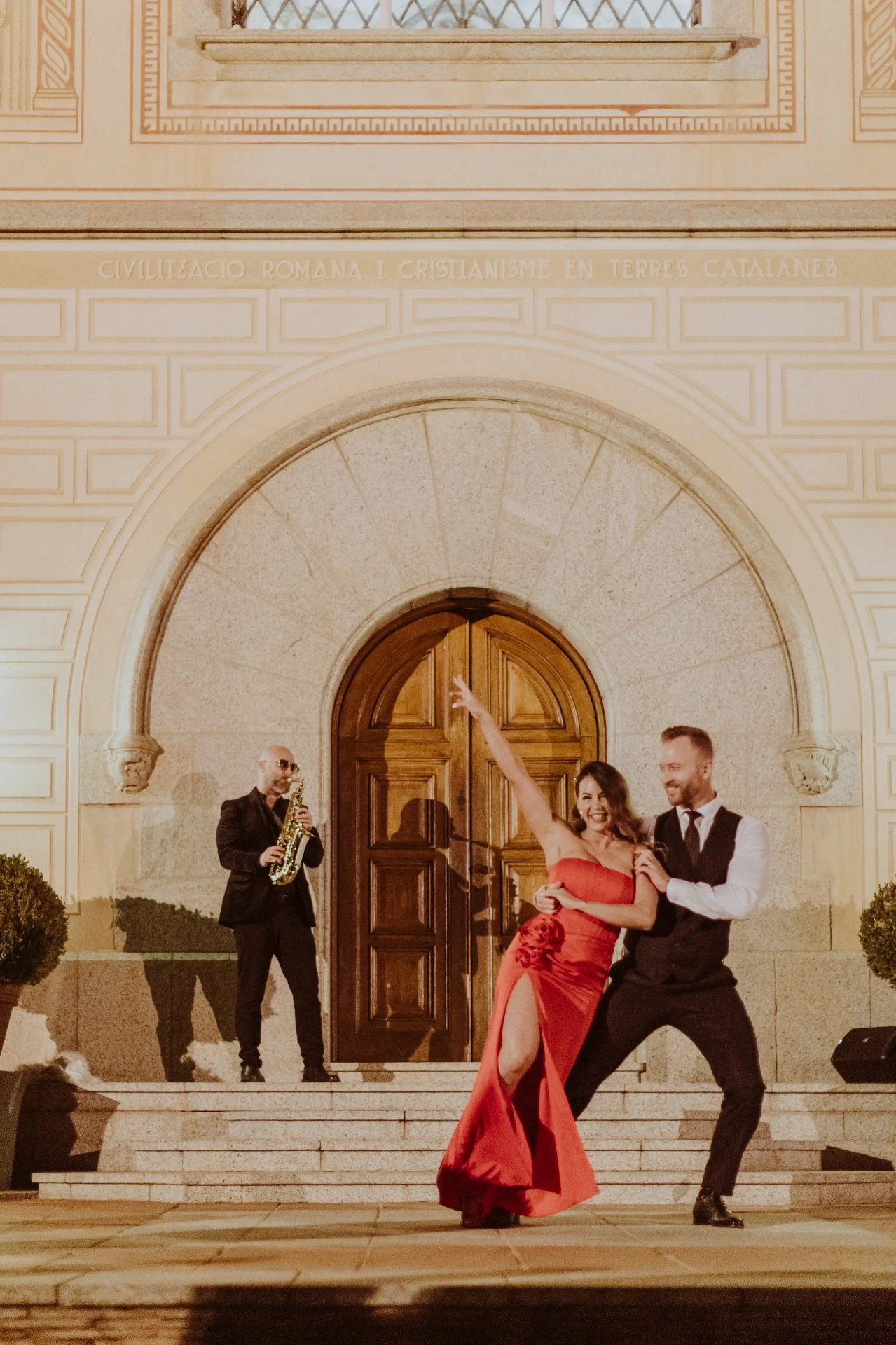 Baile de novios con vestido rojo y saxofonista en directo ante la fachada modernista de Bell Recó Argentona