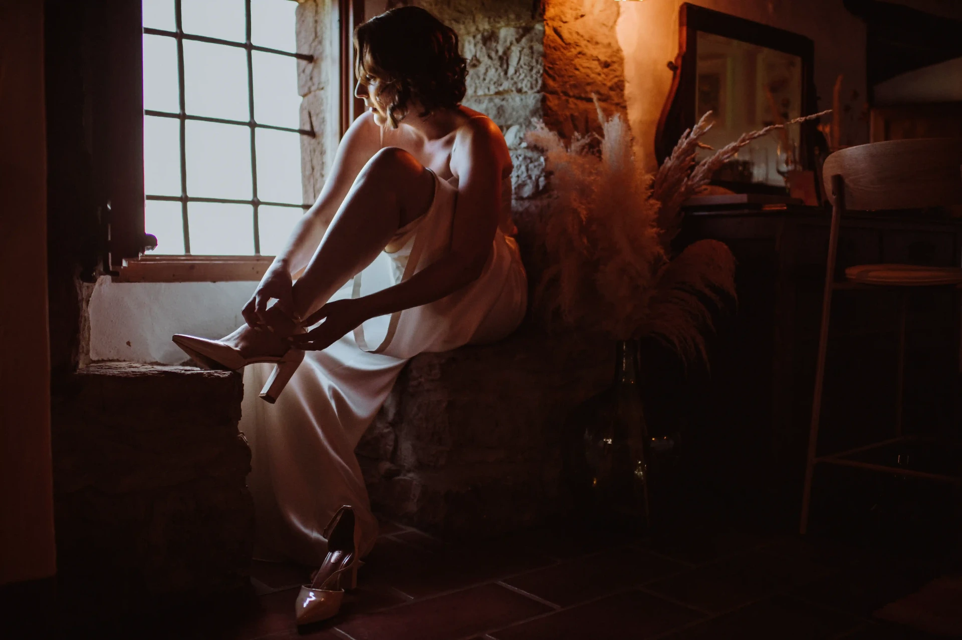 Novia atándose los zapatos junto a la ventana de piedra durante los preparativos en This Must Be The Place