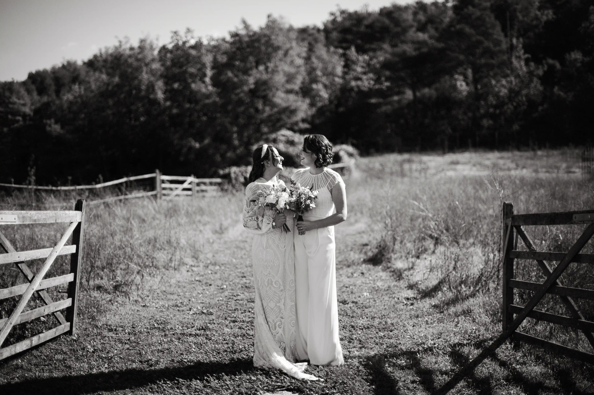 Retrato en blanco y negro de las dos novias mirándose y sonriendo junto a la puerta rústica de This Must Be The Place