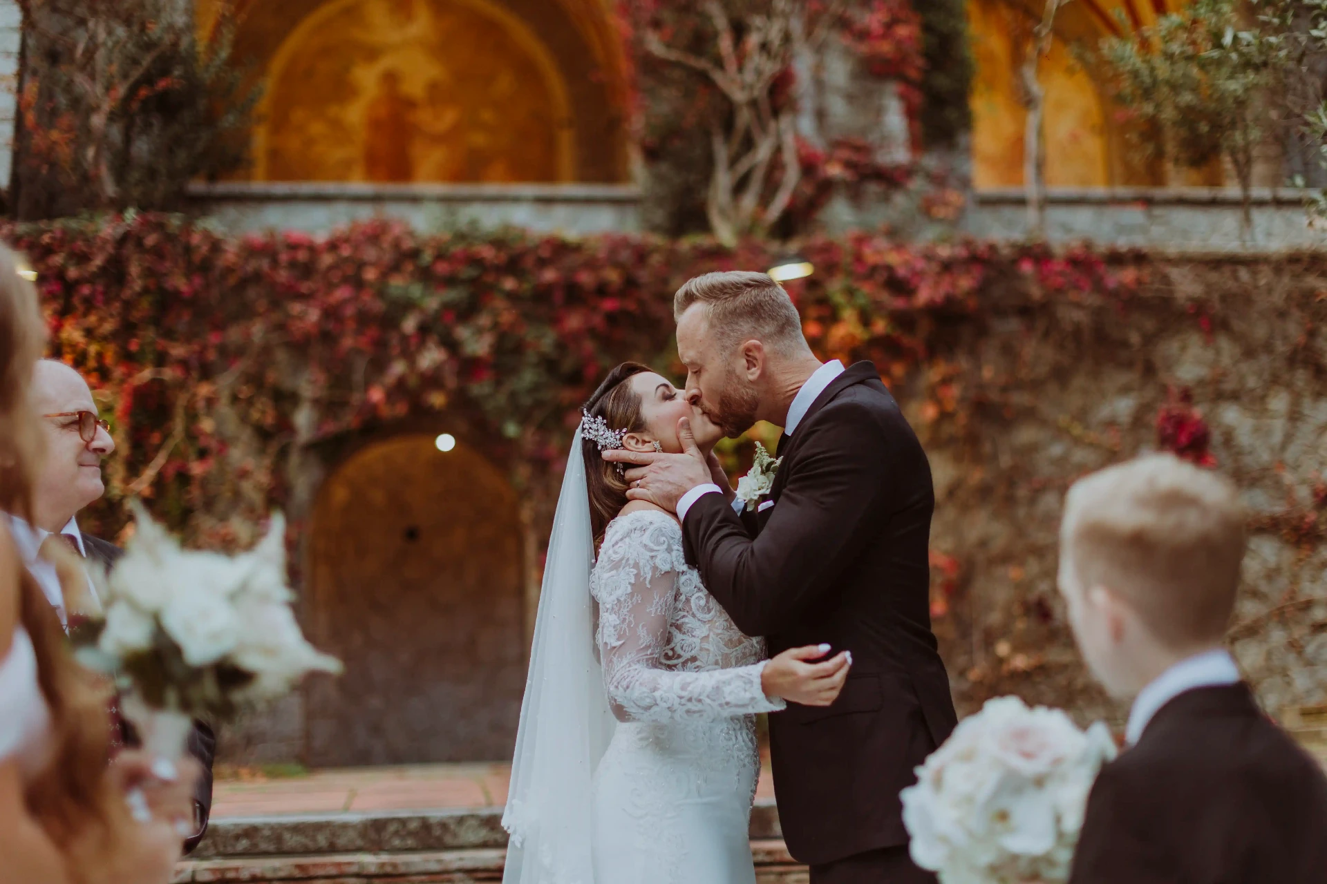 Primer beso de Lee y Ana como matrimonio ante el muro de hiedra otoñal en Bell Recó Argentona