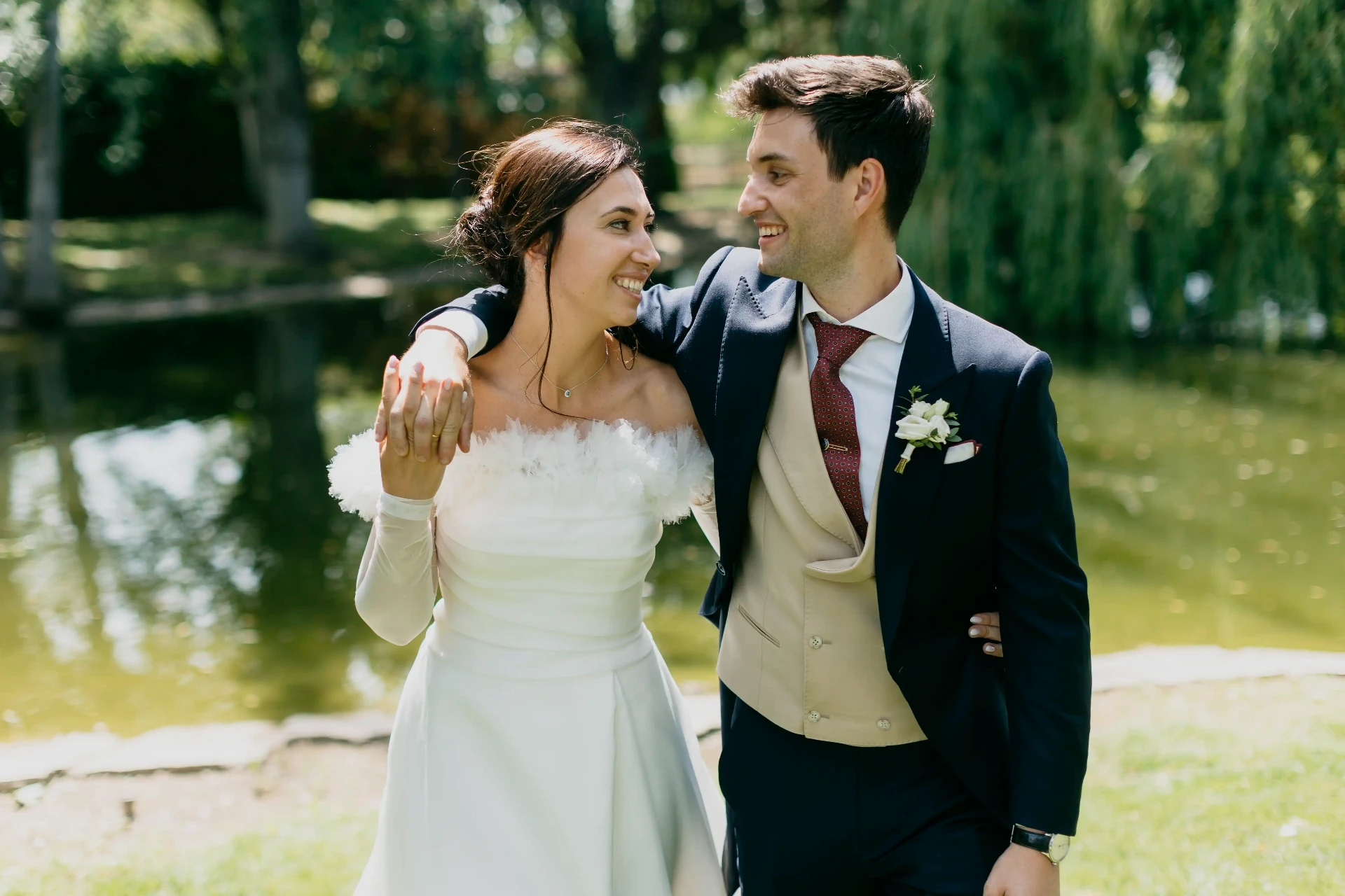 Novios paseando abrazados junto al estanque con sauces al fondo en los jardines de La Boscana, boda Bellvís Lleida