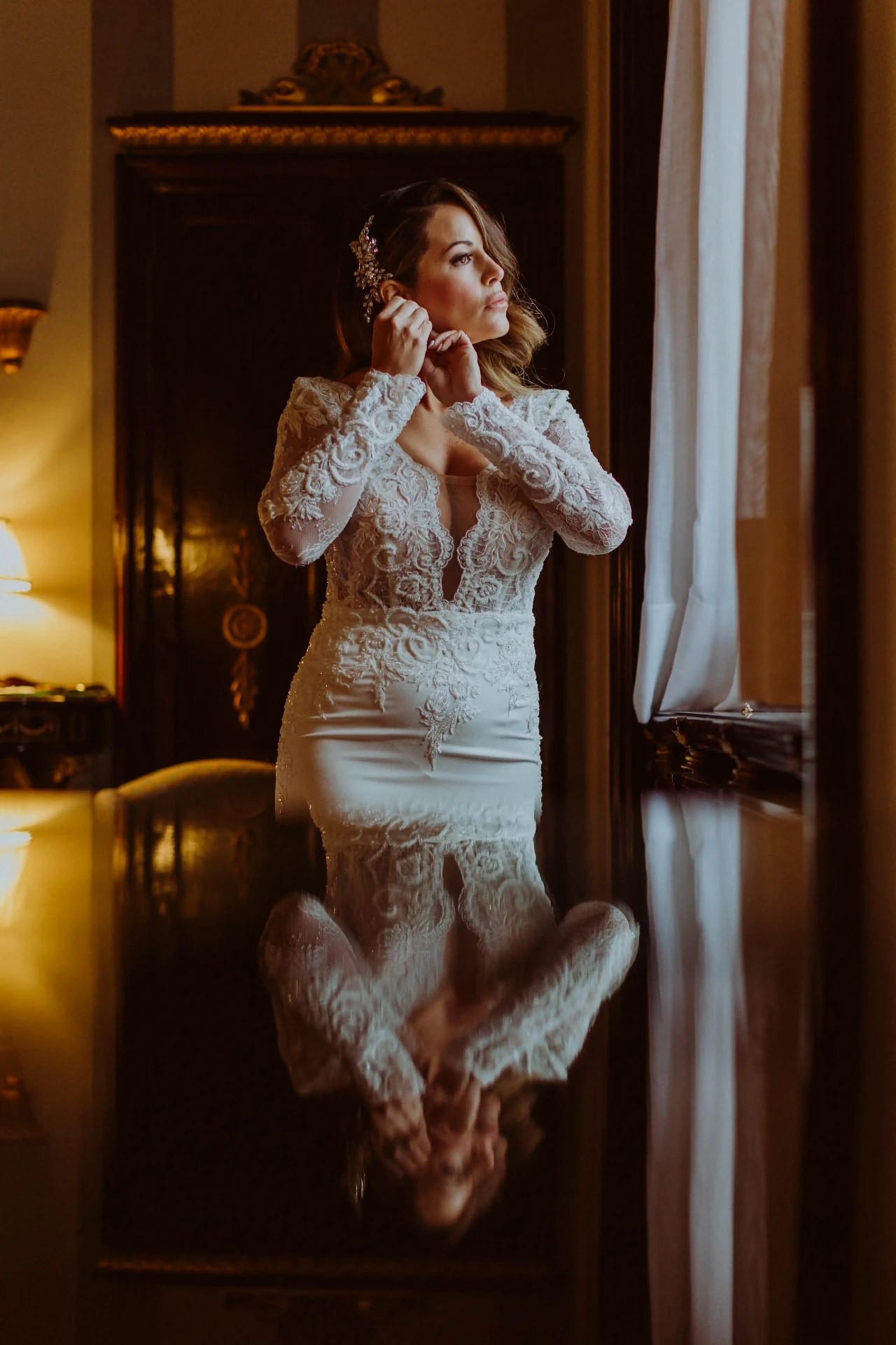 Ana con vestido de encaje poniéndose los pendientes junto a la ventana en Bell Recó