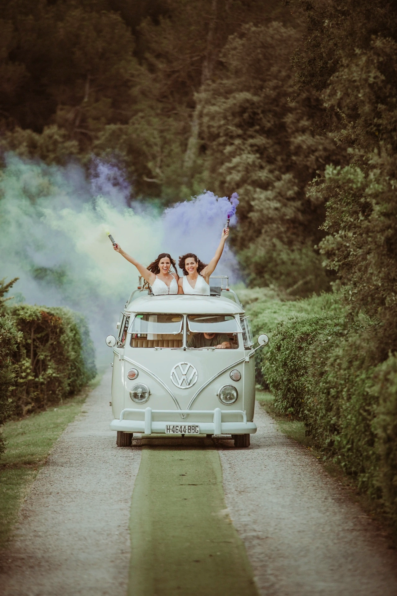 boda LGTBI en El Xaloc, Calders — las novias se alejan en una furgoneta VW por el camino entre setos con humos de colores
