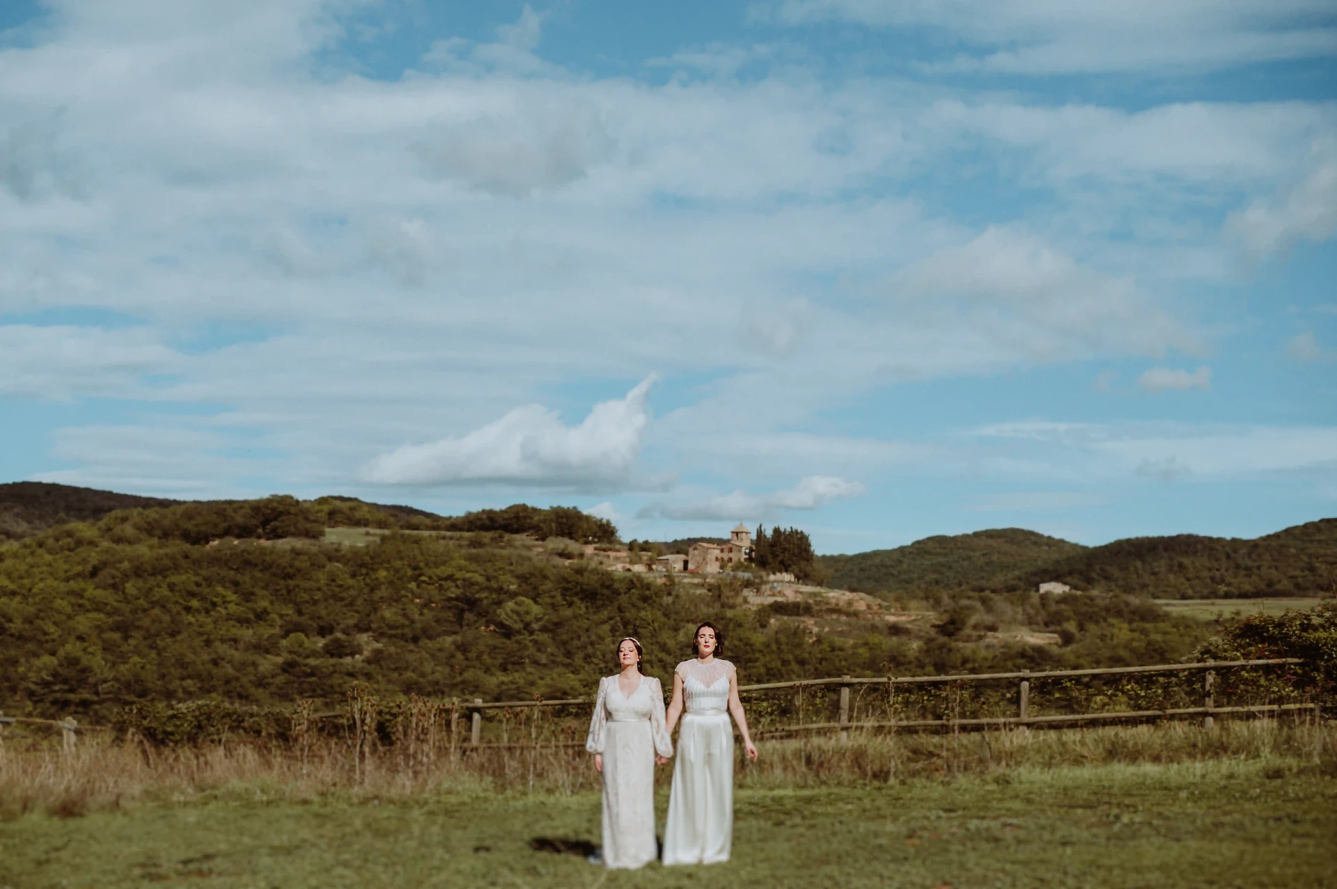 Retrato de las dos novias tomadas de la mano en la lejanía con el paisaje del Moianès al fondo desde This Must Be The Place