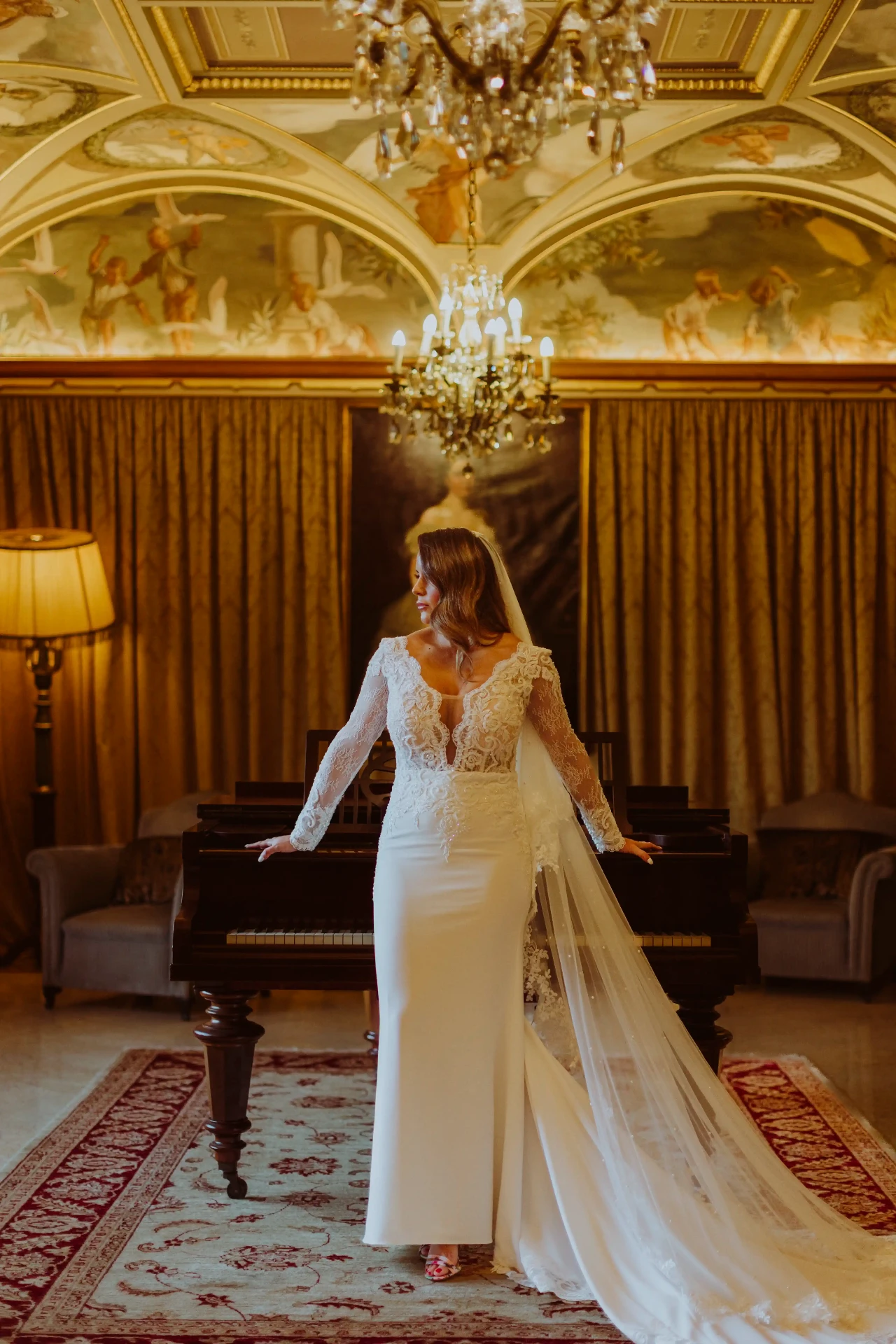 Ana con velo y cola larga junto al piano bajo los frescos del salón de Bell Recó, destination wedding cerca de Barcelona