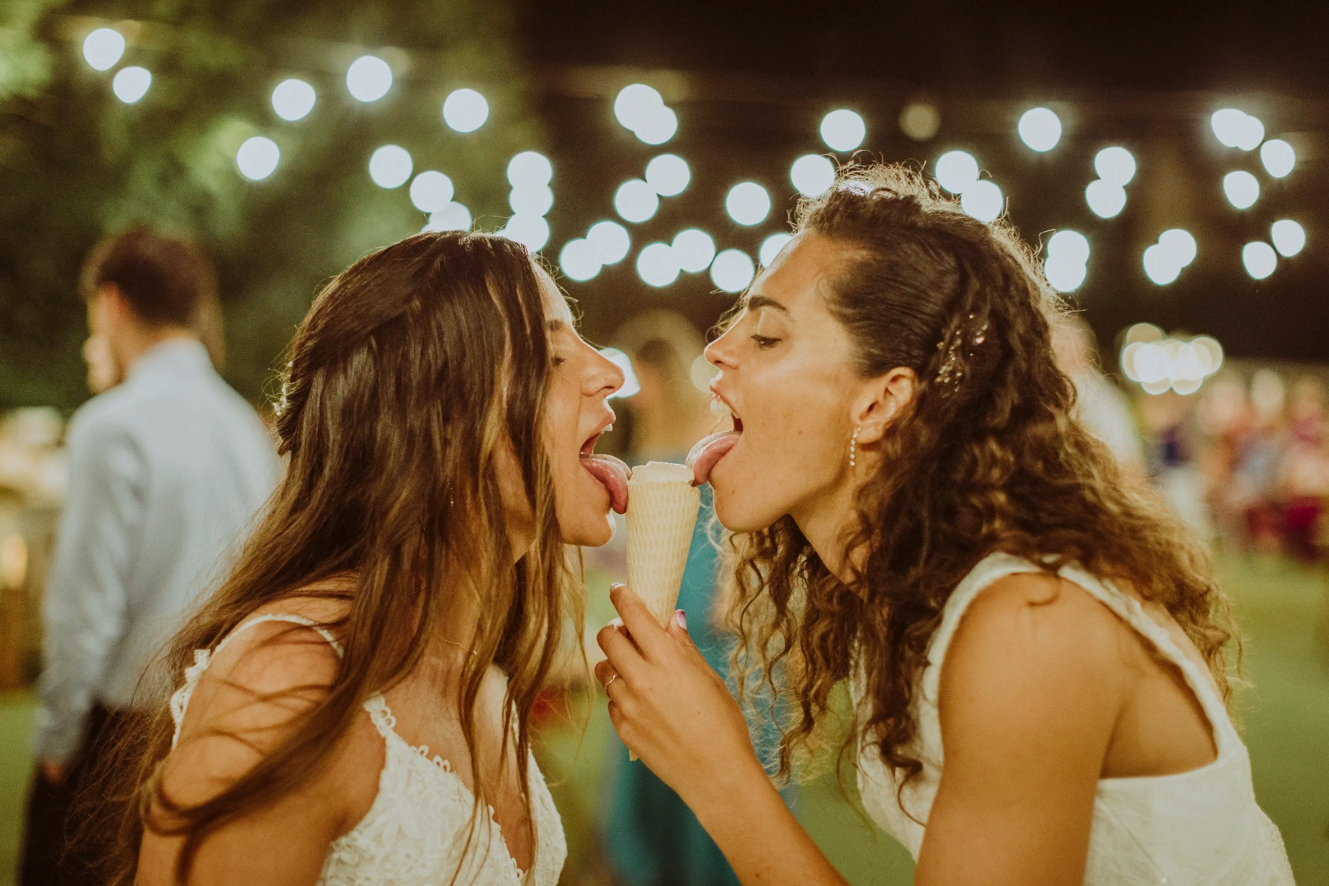 boda LGTBI en El Xaloc, Calders — las novias comparten un helado sacando la lengua bajo las guirnaldas de luces
