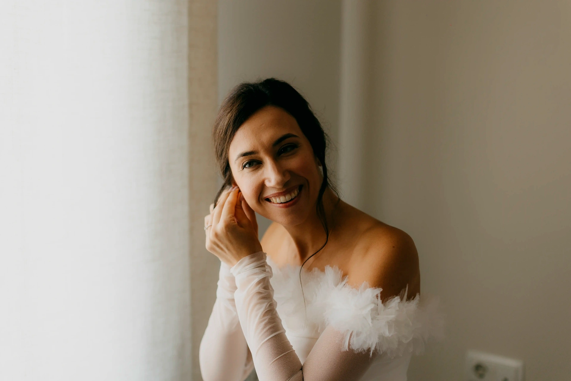 Retrato de Núria sonriendo con vestido de novia junto a la ventana, preparativos boda La Boscana