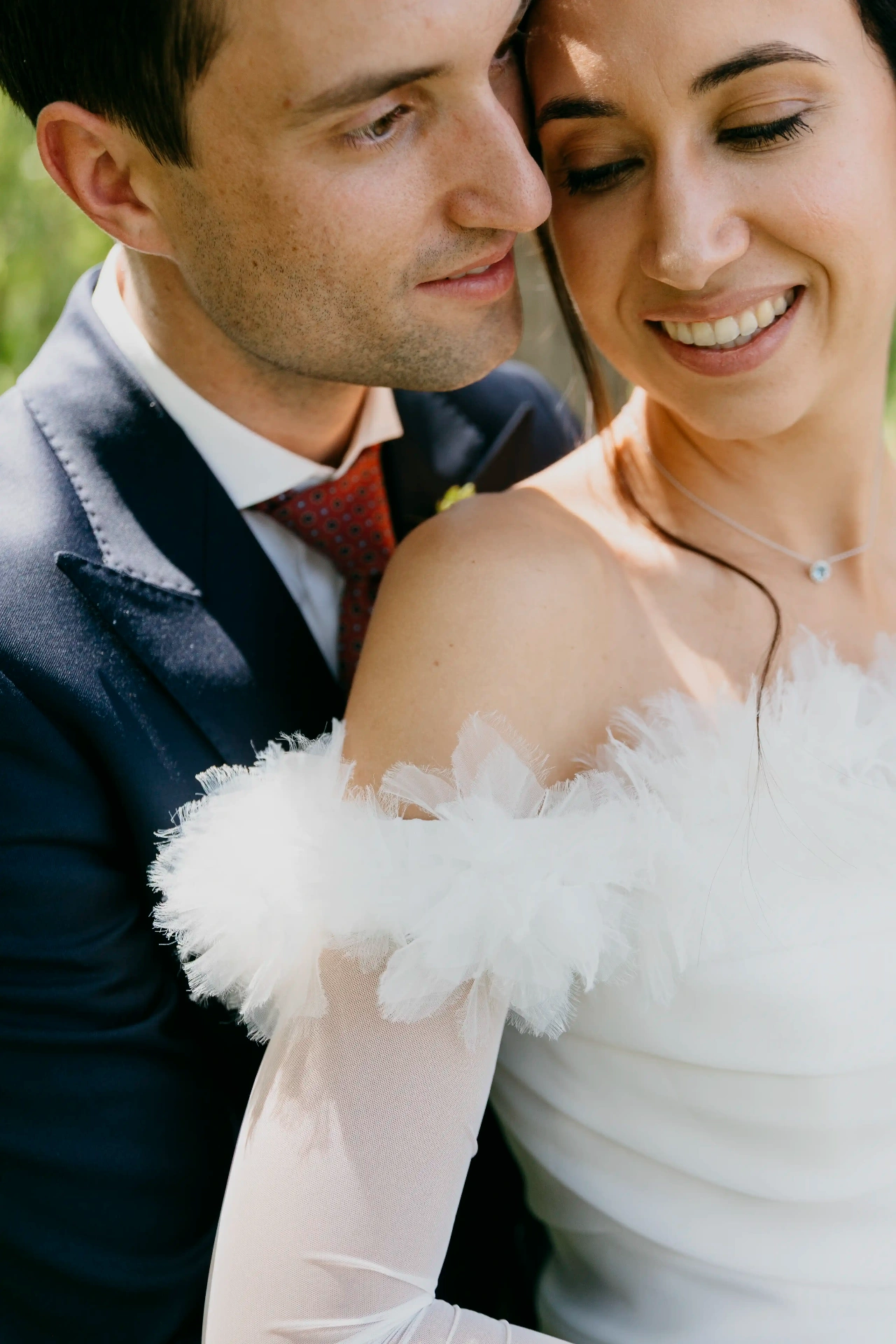 Primer plano de novia sonriendo con vestido de tul plumas mientras el novio le apoya la cabeza, boda La Boscana Lleida