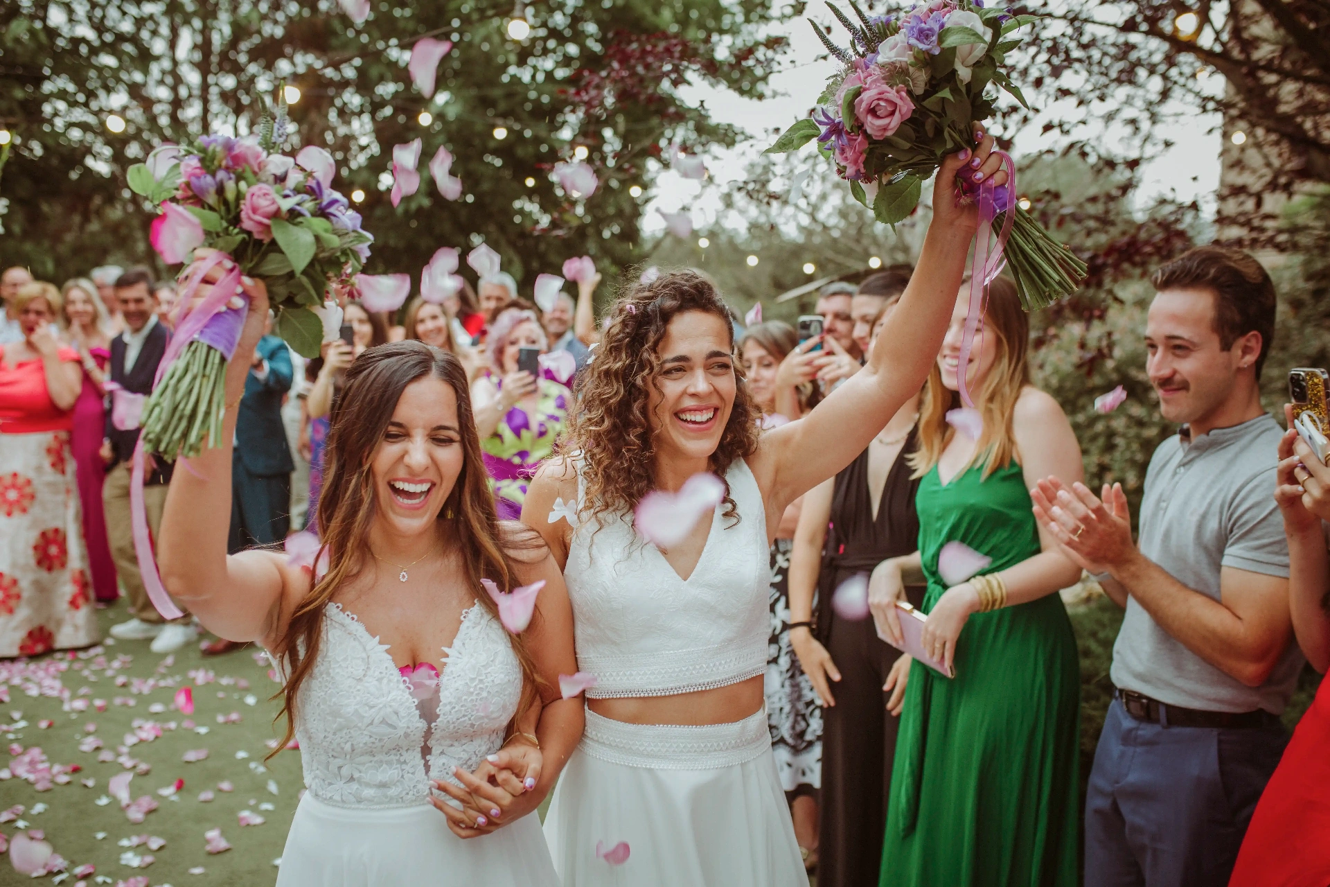 boda LGTBI en El Xaloc, Calders — las novias levantan los ramos entre risas mientras los invitados lanzan pétalos