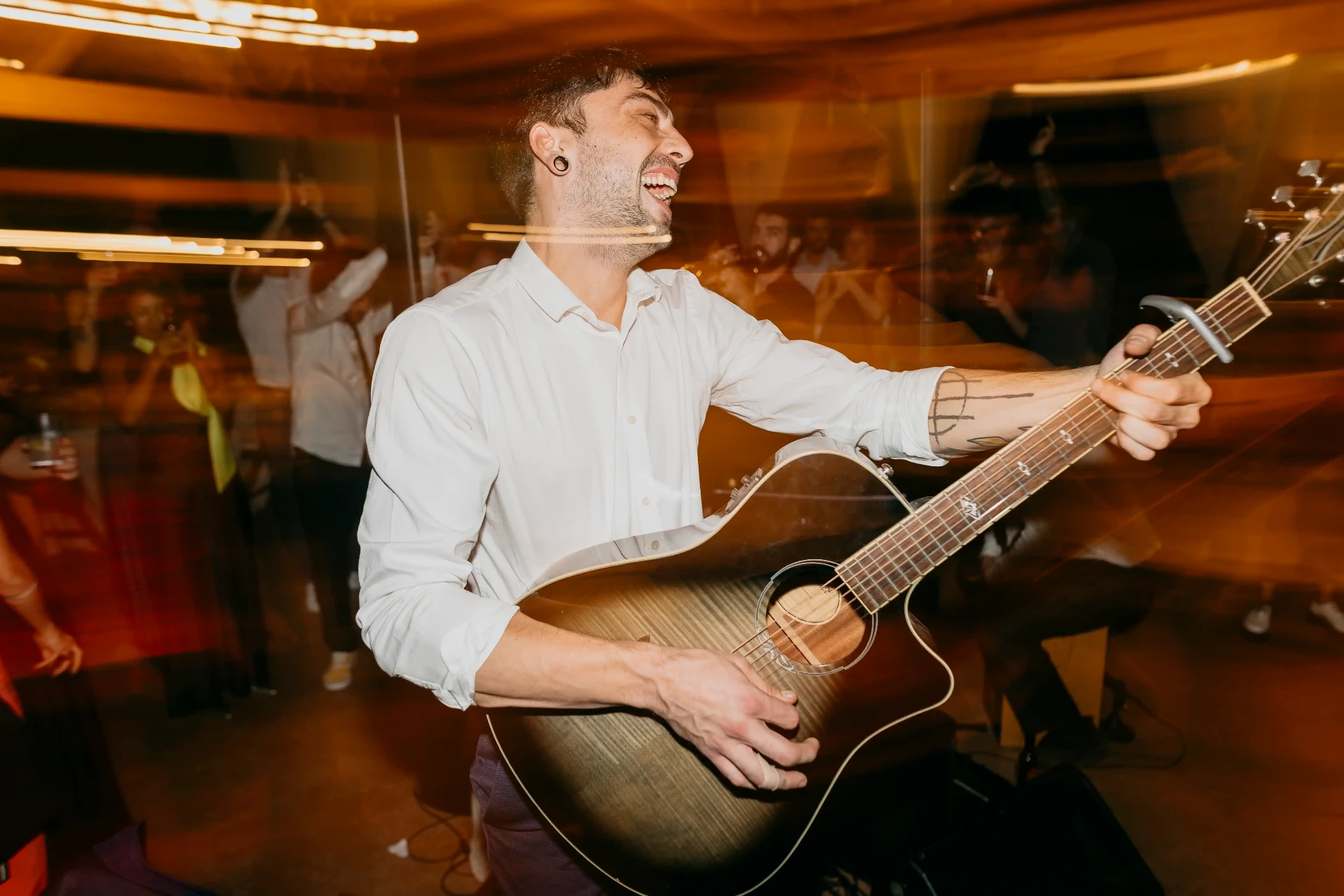 Guitarrista cantando y sonriendo entre luces cálidas durante el concierto en directo en la boda de Can Riera de la Pineda
