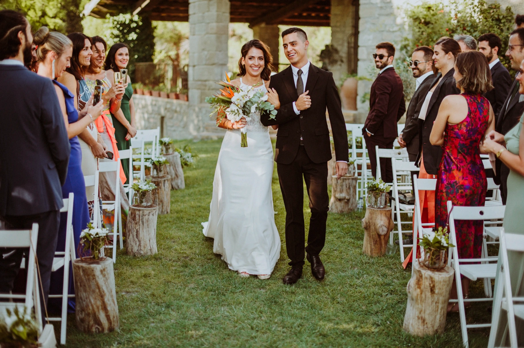 boda LGTBI en Ca n'Alzina — la otra novia entrando a la ceremonia con ramo tropical y traje oscuro