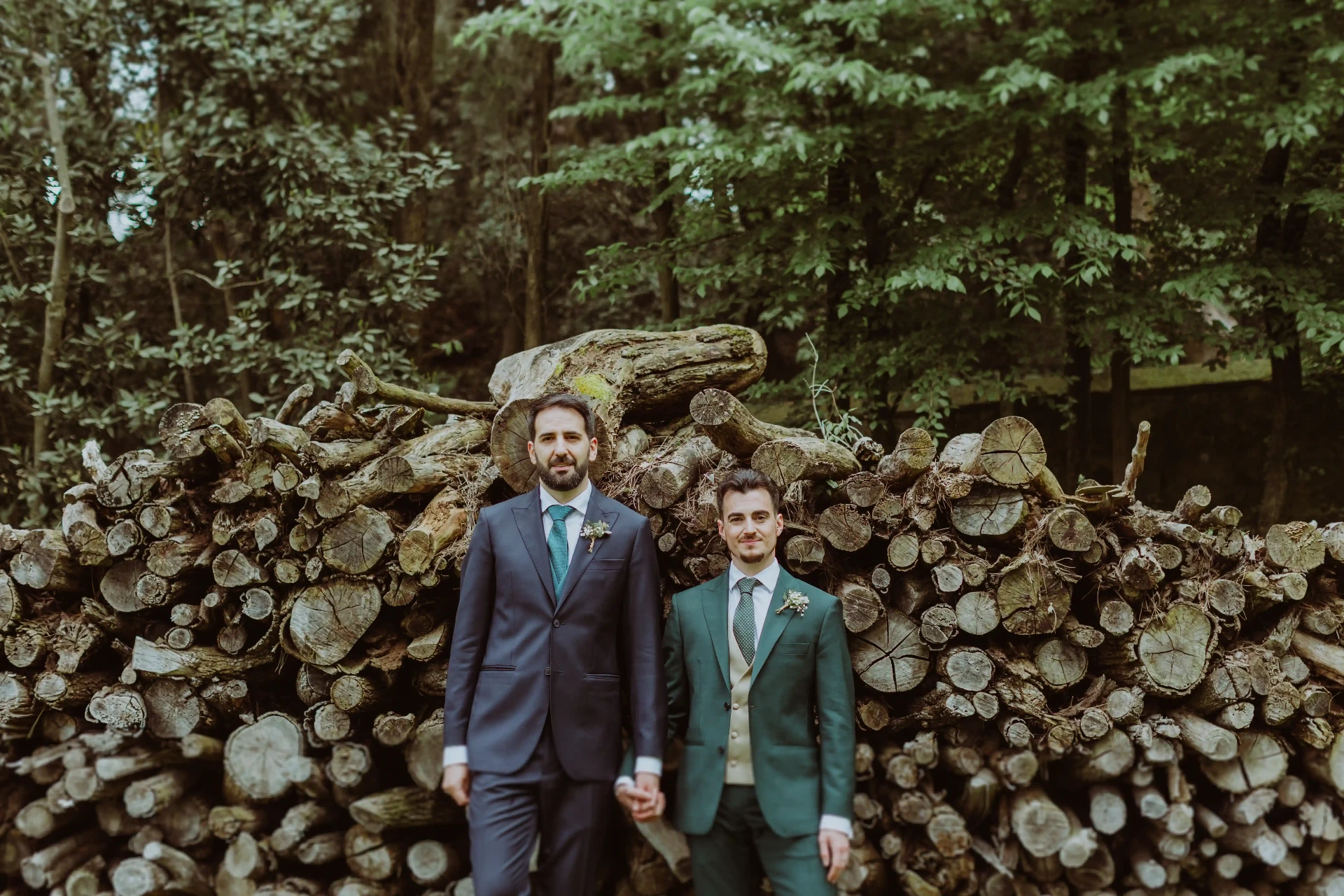 boda LGTBI en Can Ribas — retrato de los novios frente a leña apilada en el bosque