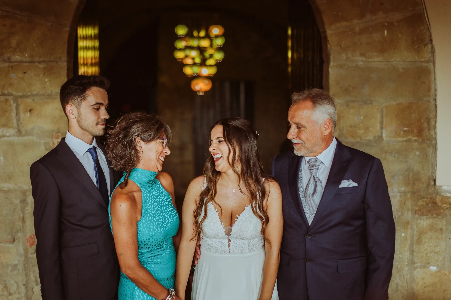 boda LGTBI en El Xaloc, Calders — la novia ríe con sus padres y su hermano bajo un arco de piedra