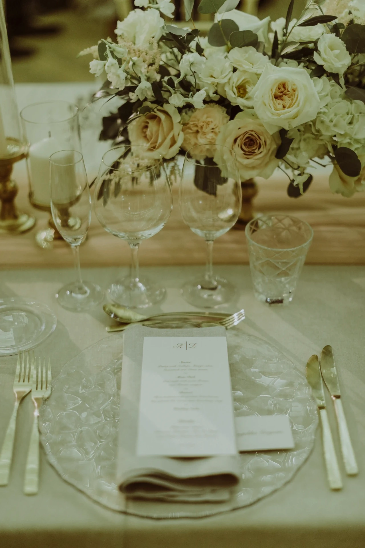 Detalle editorial del montaje de mesa con menú, cristalería y centro floral de rosas blancas en Bell Recó