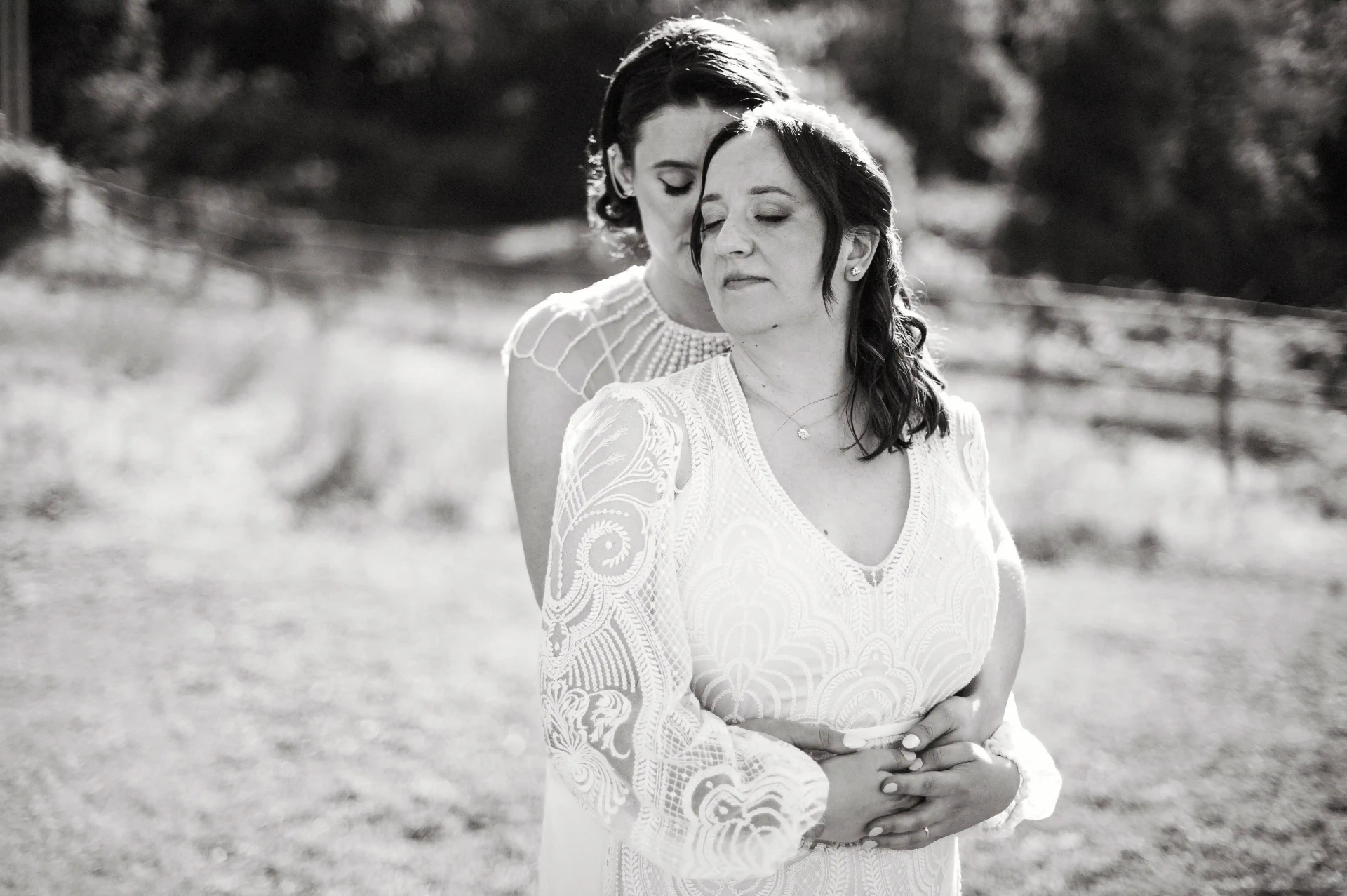 Retrato íntimo en blanco y negro de las dos novias abrazadas en el campo de This Must Be The Place