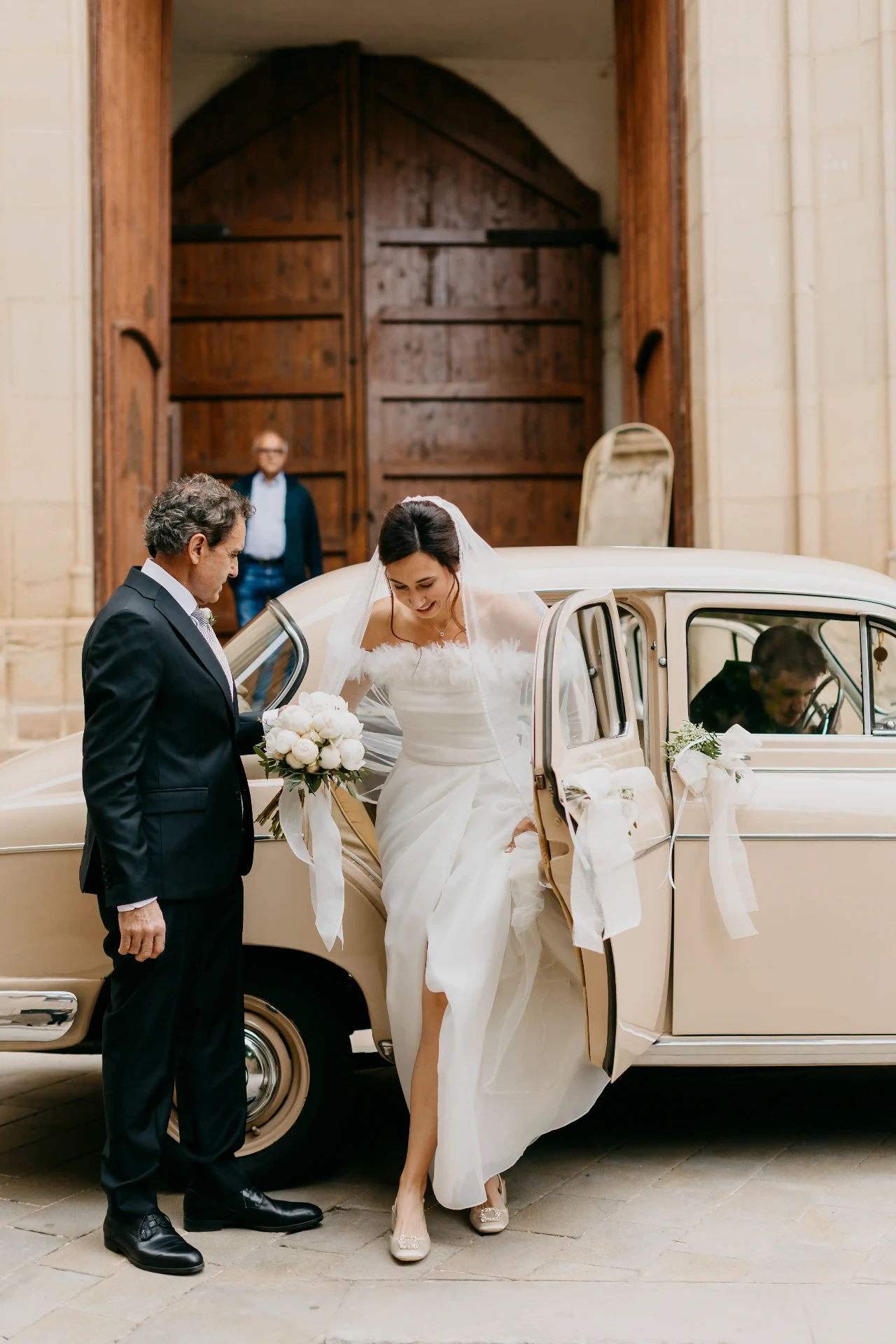 Novia bajando del coche clásico ayudada por su padre a la puerta de Santa Maria de Cervera, boda Lleida