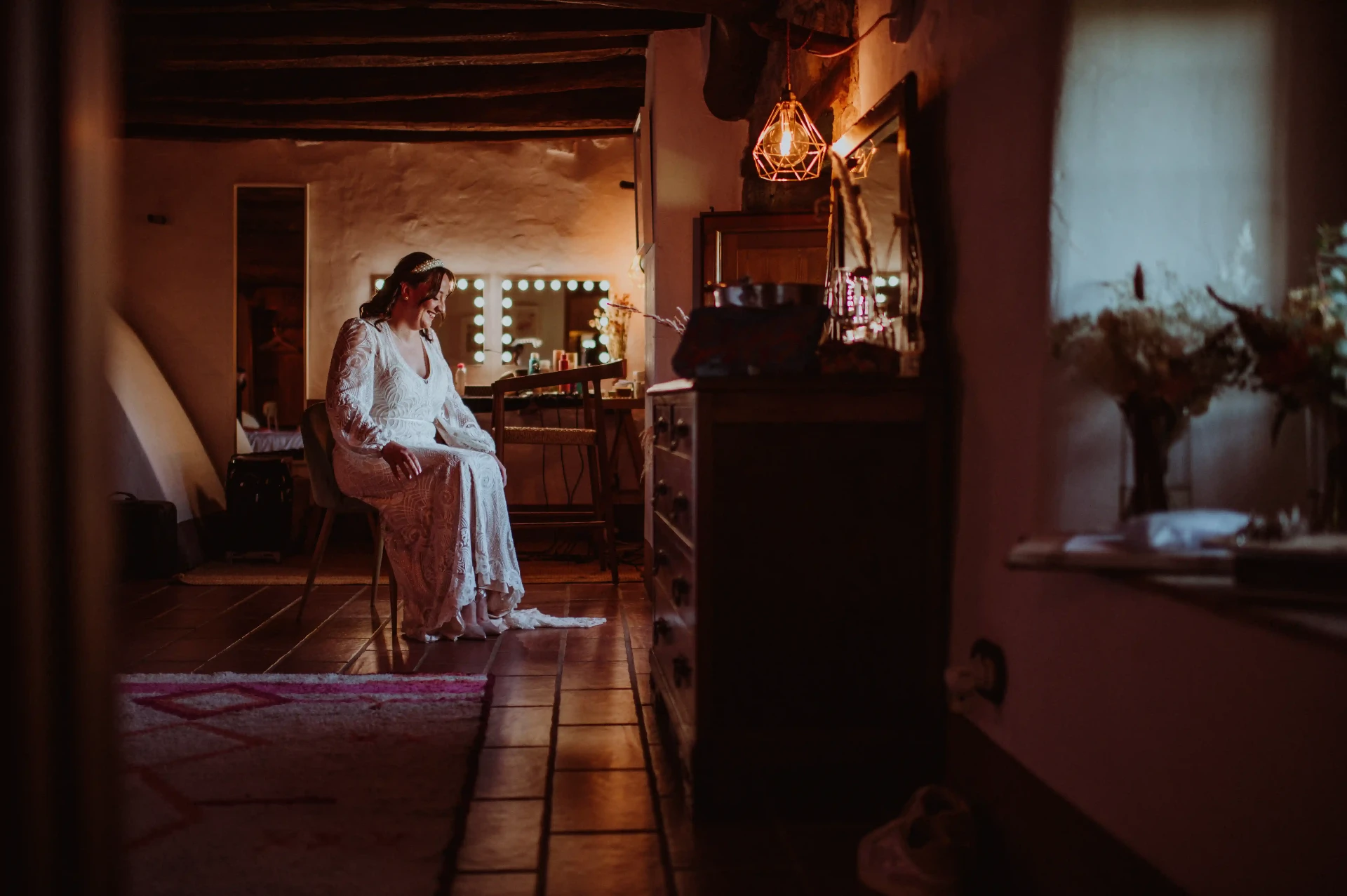 Novia sentada sonriendo junto al tocador iluminado en la habitación de preparativos de This Must Be The Place