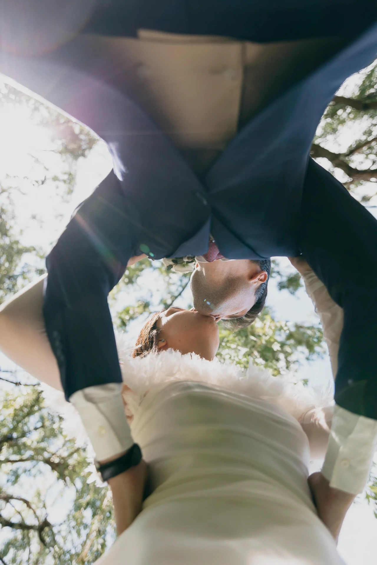 Beso de novios visto en contrapicado con destello solar entre las hojas de los árboles, boda La Boscana Lleida