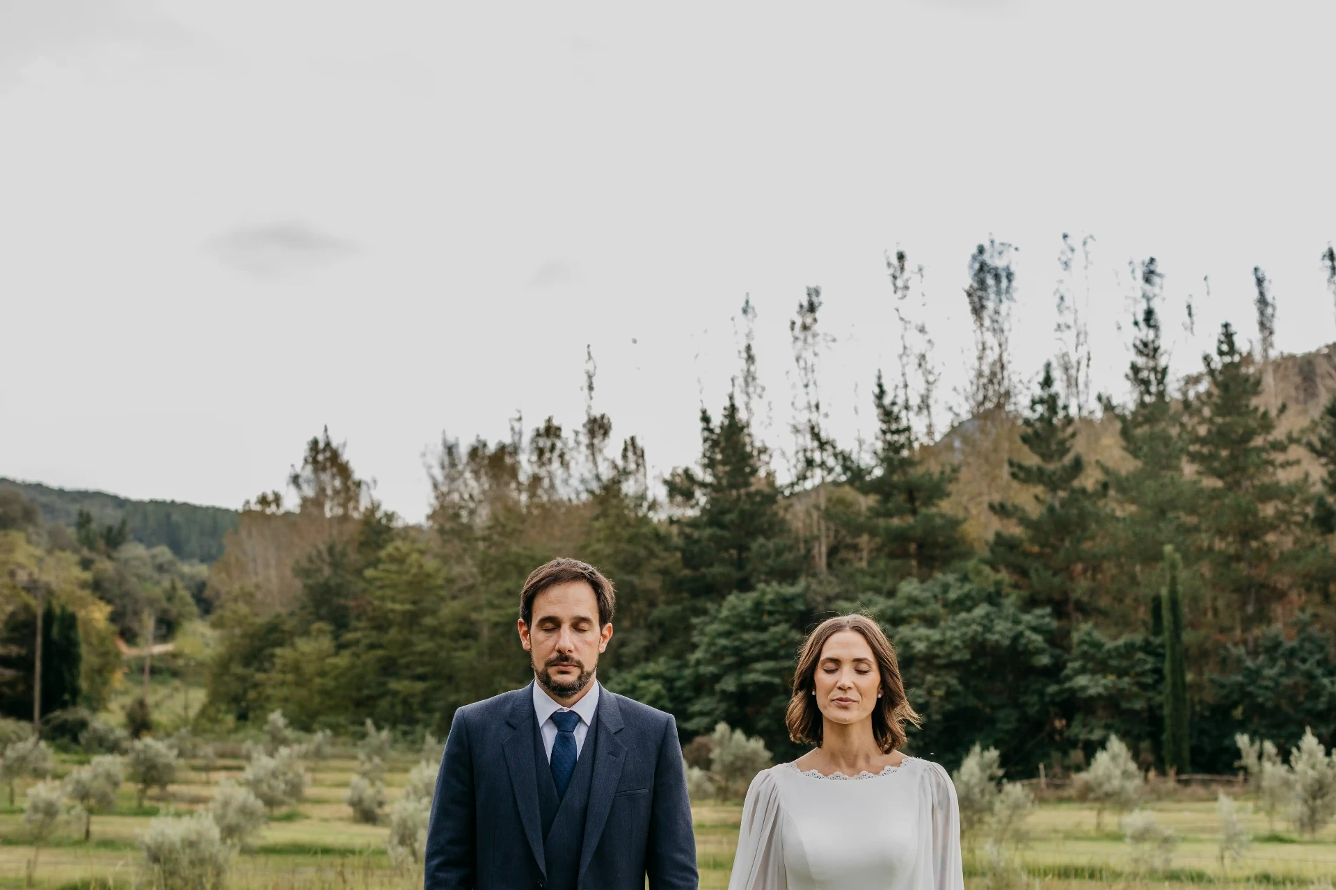 Retrato de pareja de Carla y Dani con ojos cerrados frente al bosque y olivos del Montseny en Can Riera de la Pineda
