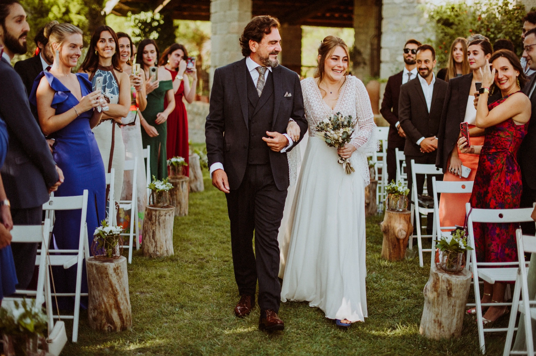 boda LGTBI en Ca n'Alzina (Rubió) — una de las novias entrando a la ceremonia del brazo de su padre entre los invitados