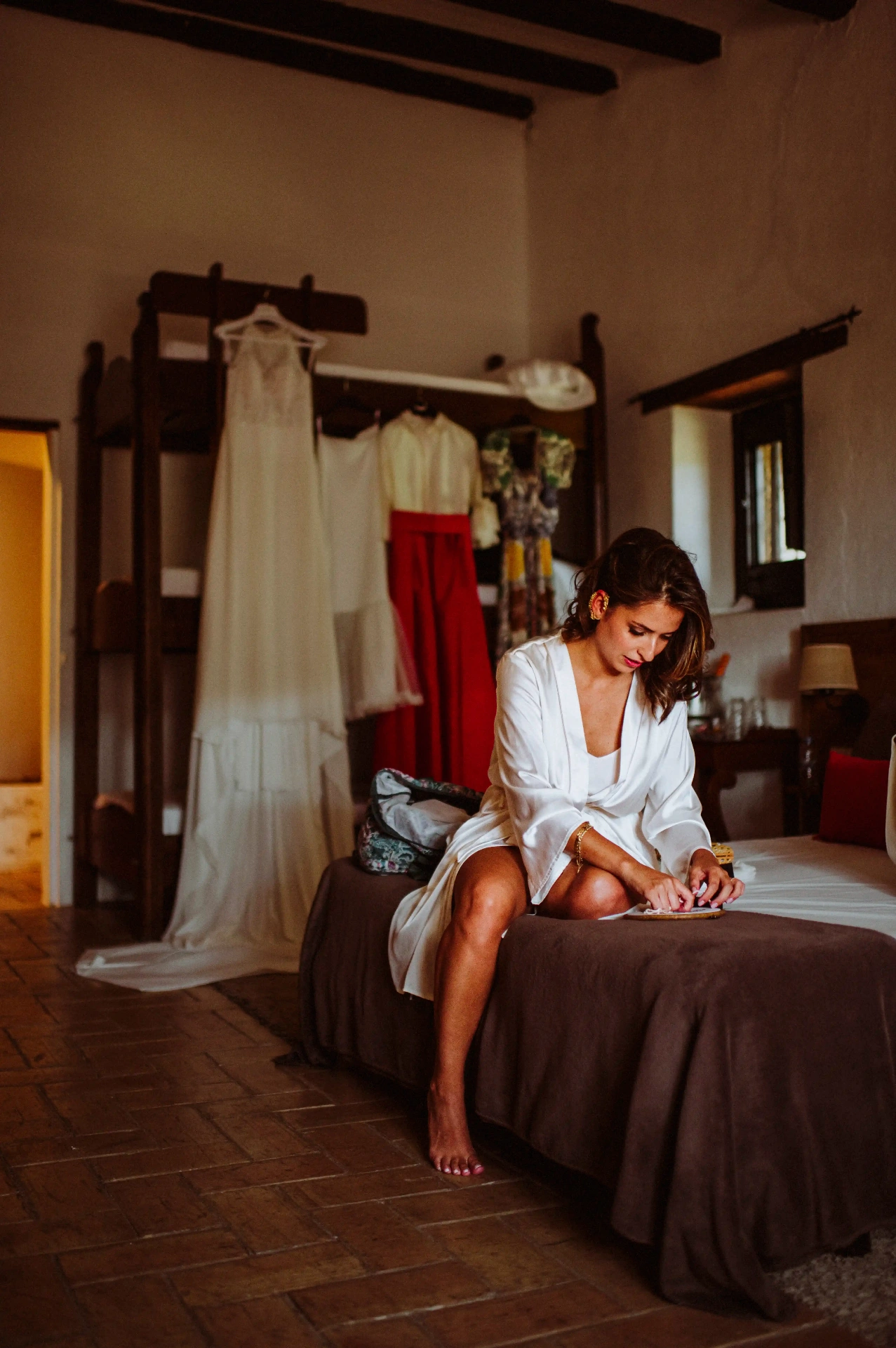 boda LGTBI en Ca n'Alzina — novia arreglándose en la habitación de la masía con el vestido colgado al fondo