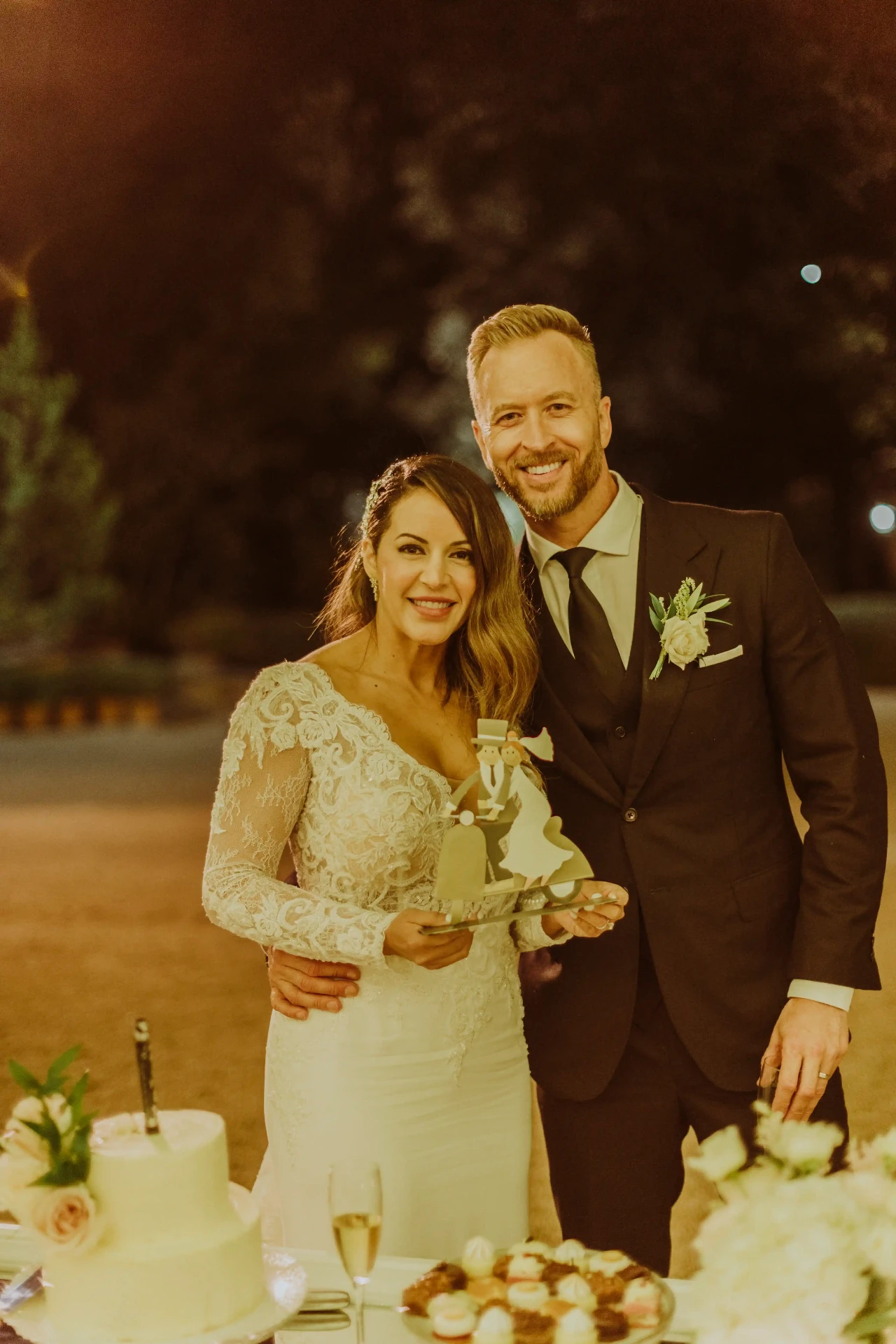 Retrato de Ana y Lee sonrientes junto a la mesa dulce y tarta nupcial en Bell Recó Argentona