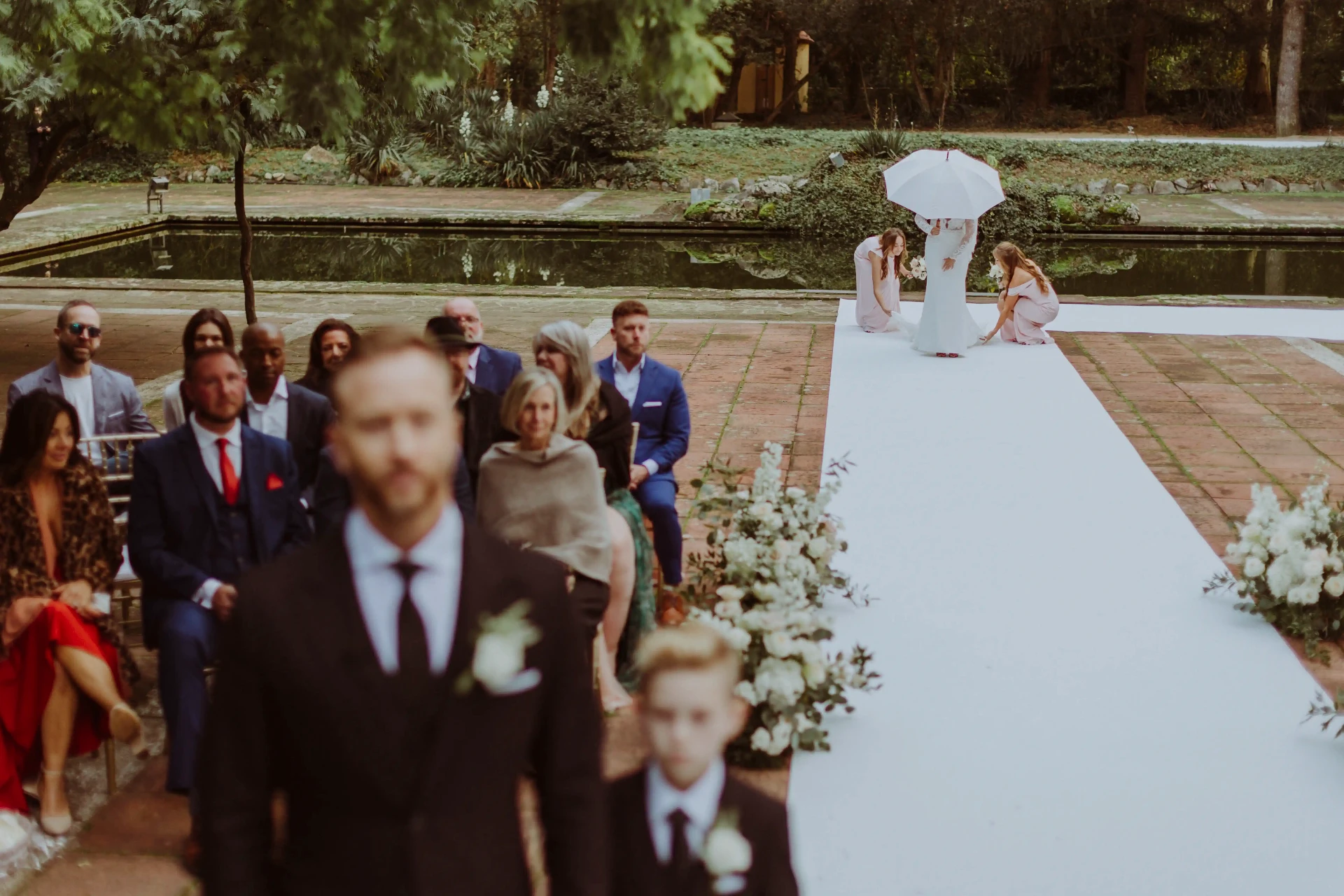 Ana llegando al altar bajo un paraguas blanco reflejada en el estanque de Bell Recó