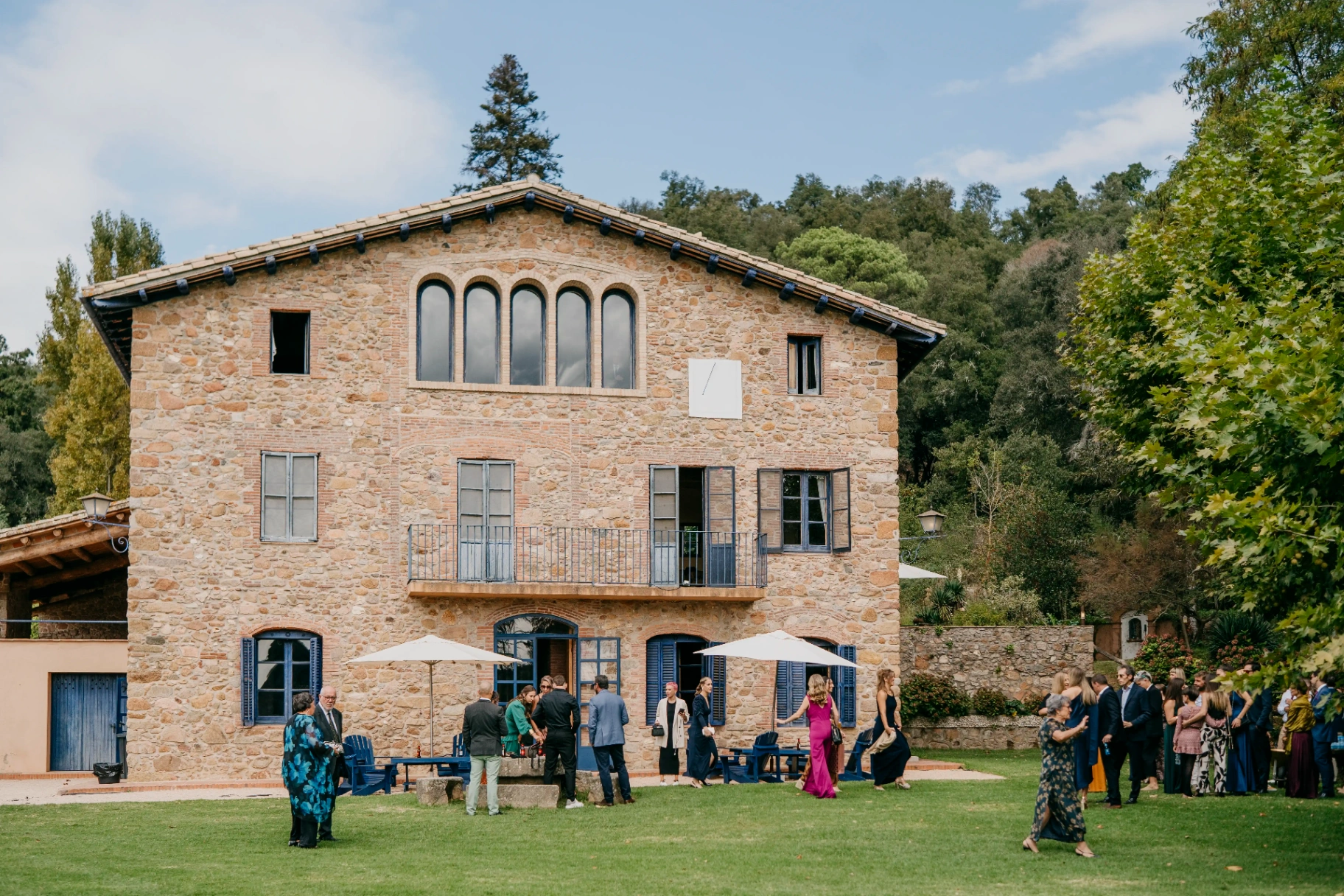 Fachada de piedra de la masía Can Riera de la Pineda con invitados llegando al aperitivo en el jardín del Montseny