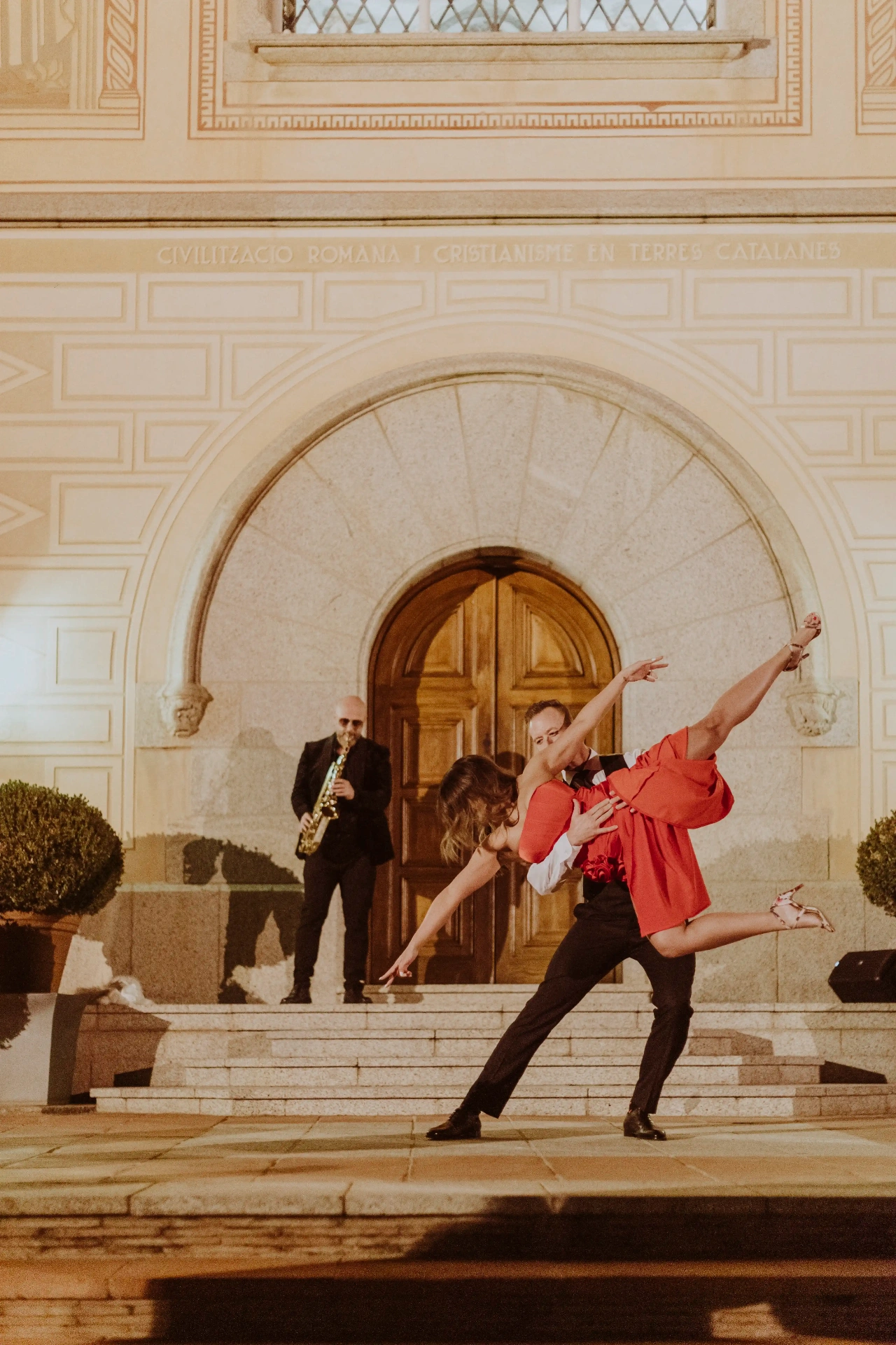 Coreografía de baile con salto y saxofonista en directo bajo el arco iluminado de Bell Recó Argentona