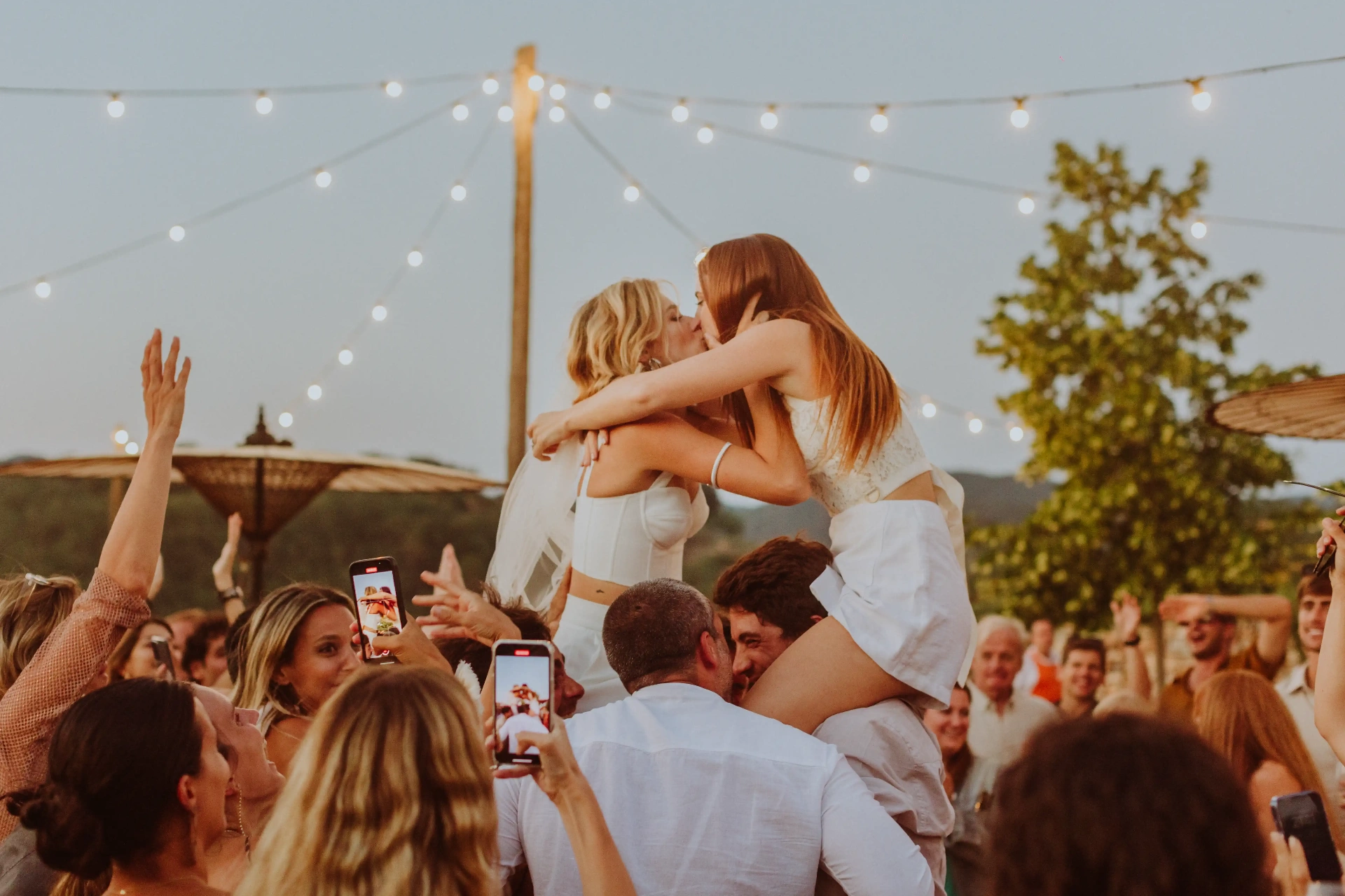 Boda LGTBI: dos novias besándose sobre los hombros de los invitados en la fiesta en This Must Be The Place, Moià. Piña Colada