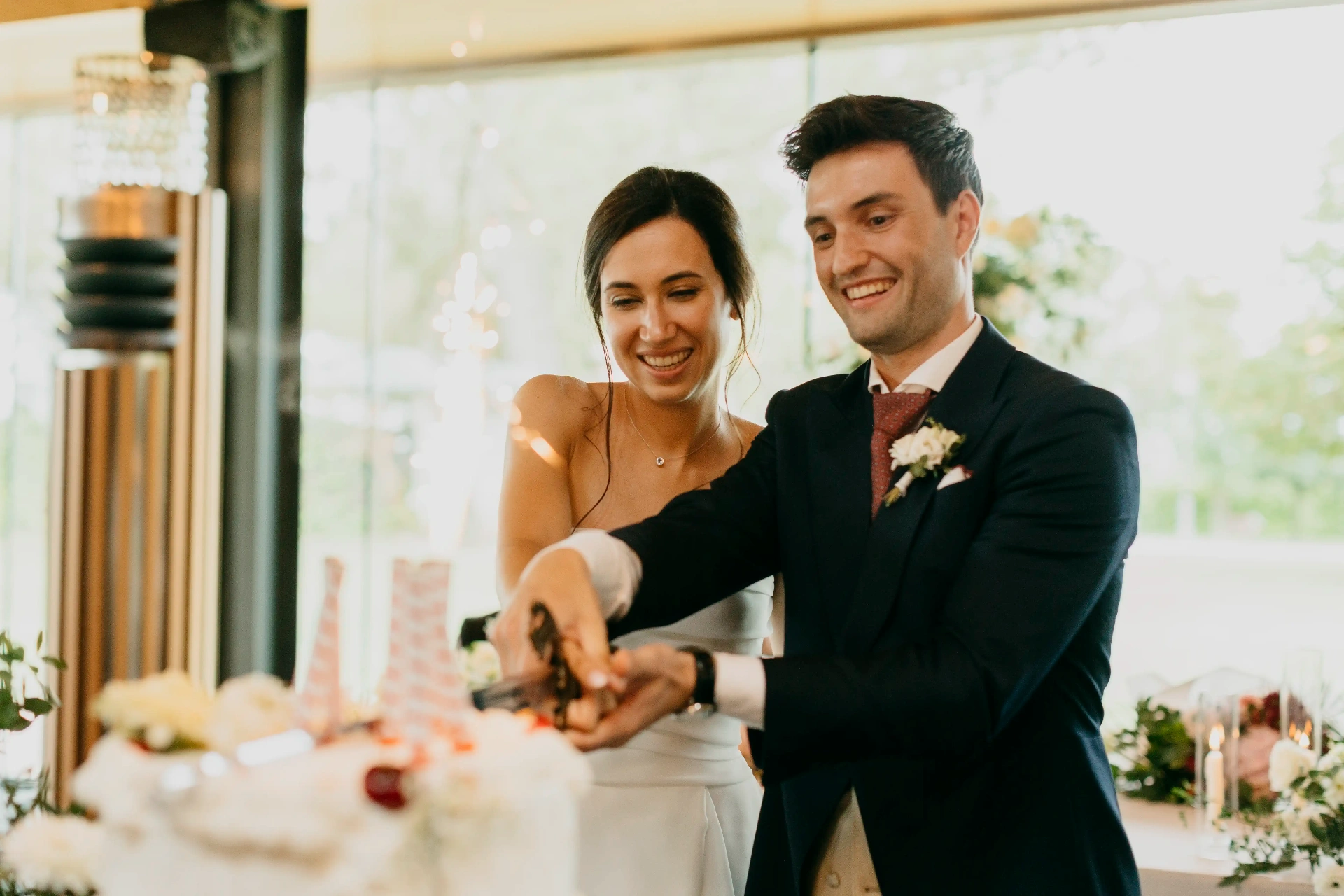 Novios cortando la tarta nupcial entre bengalas junto a los ventanales del salón de La Boscana, boda Lleida