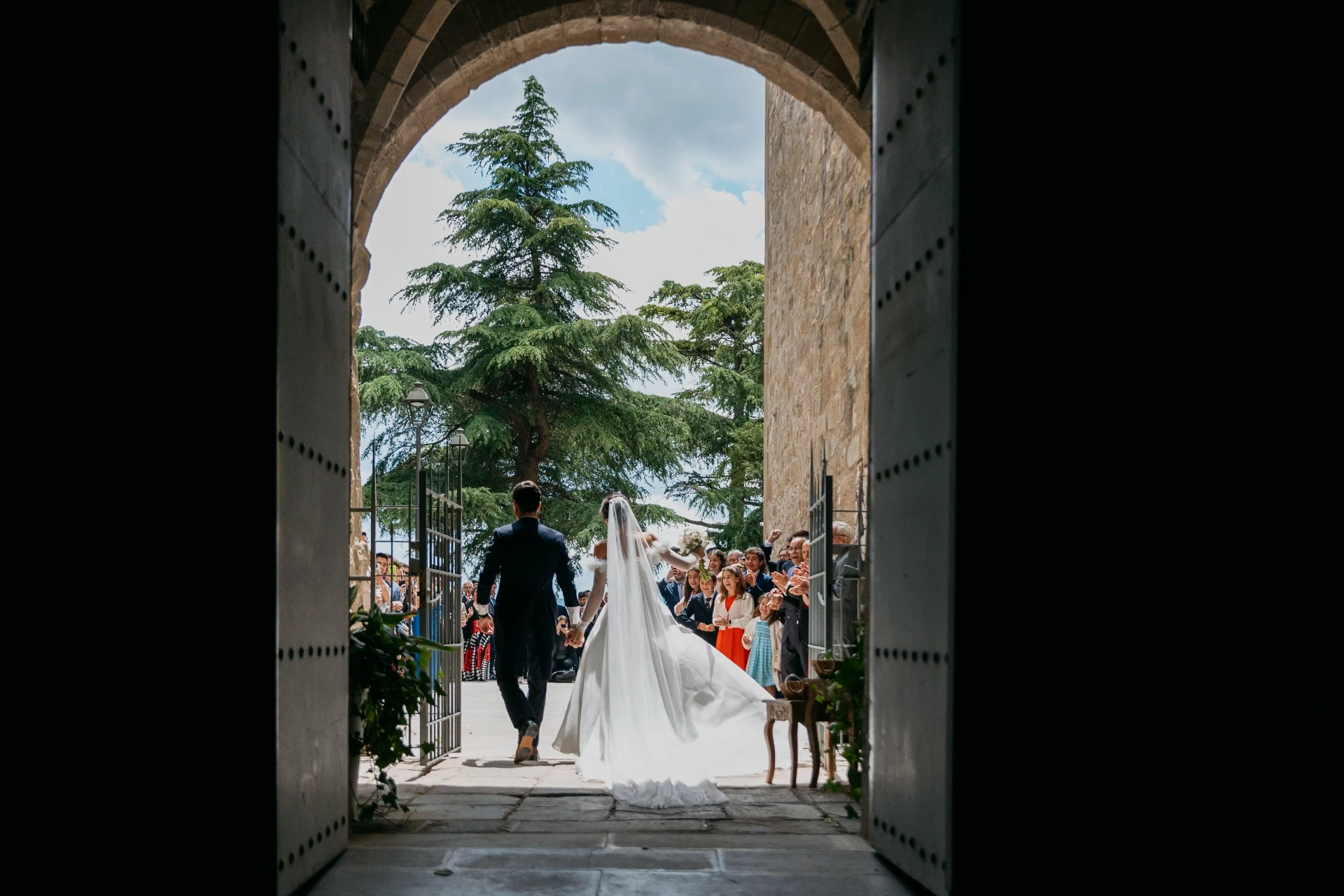 Salida de los novios por el arco de piedra de Santa Maria de Cervera con invitados aplaudiendo, boda La Boscana Lleida