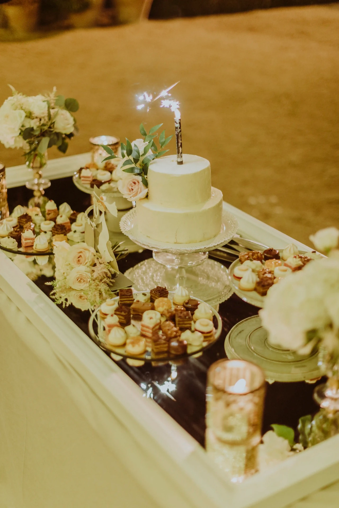 Mesa dulce con tarta nupcial, petit fours y bengala durante la boda nocturna en Bell Recó Argentona