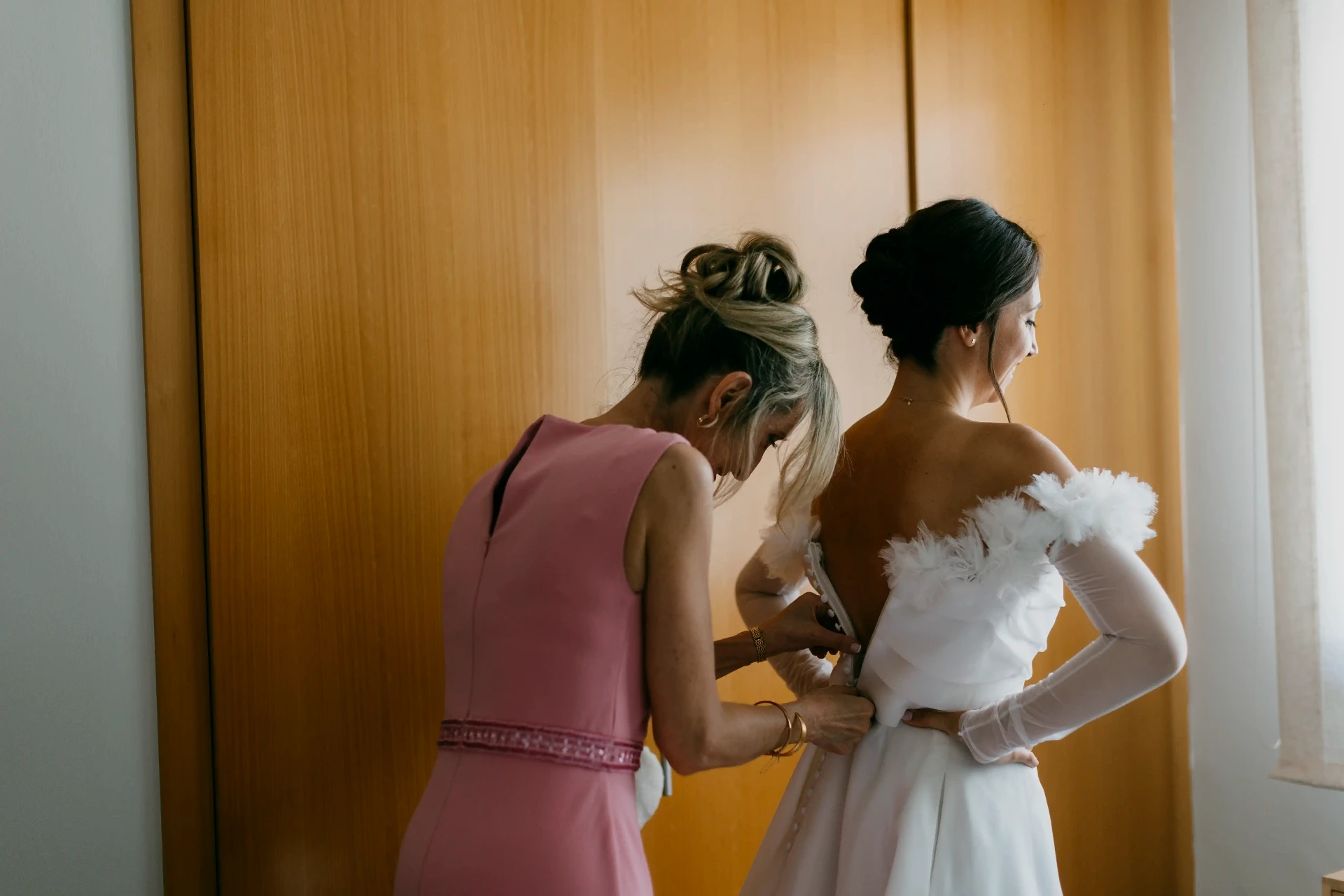 Madre abrochando el vestido de novia con hombros descubiertos y tul, preparativos boda Lleida
