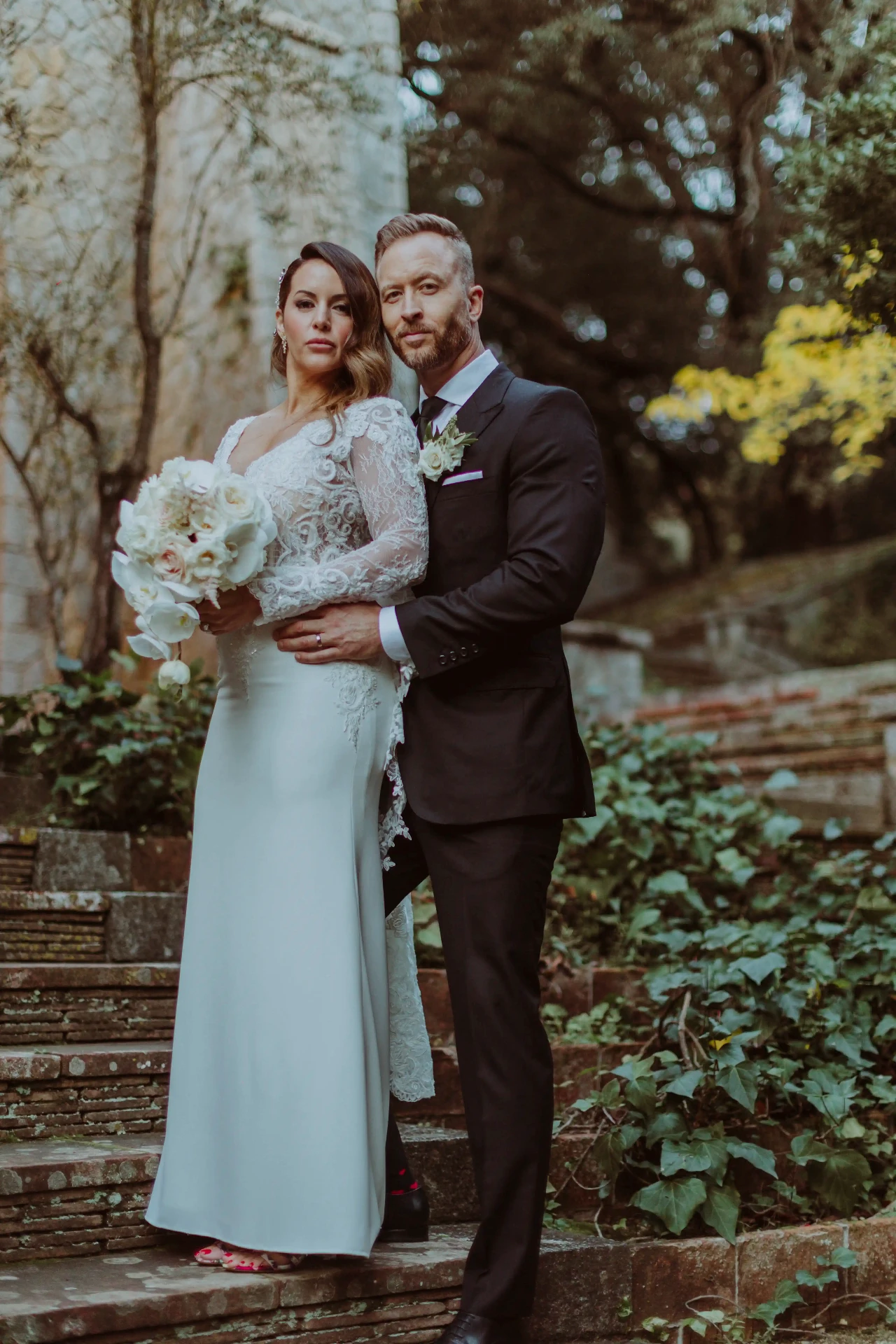 Ana y Lee abrazados en las escaleras del jardín de Bell Recó al atardecer, destination wedding cerca de Barcelona