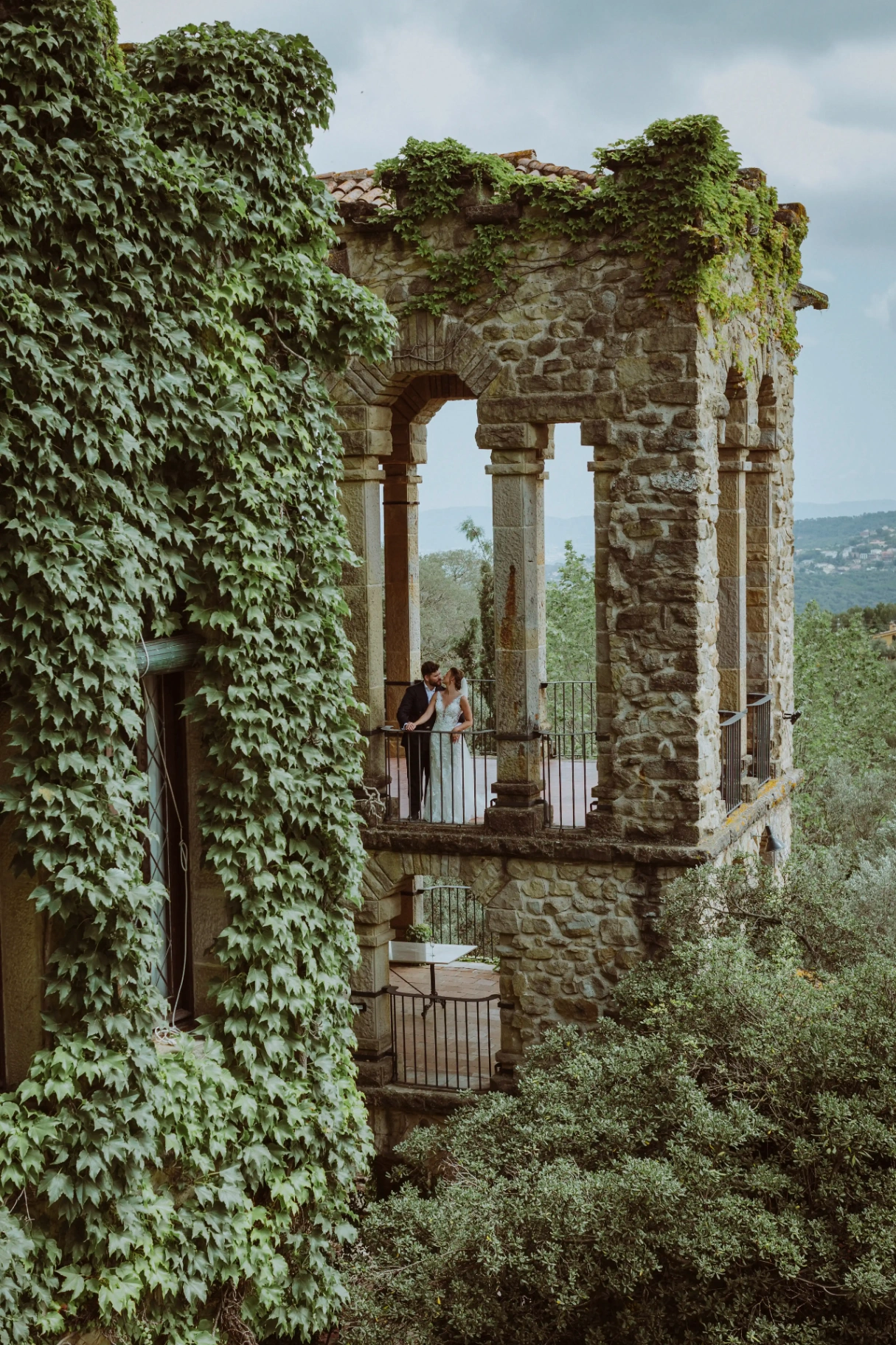 Los novios en el balcón de piedra e hiedra de La Baronia con vistas al valle