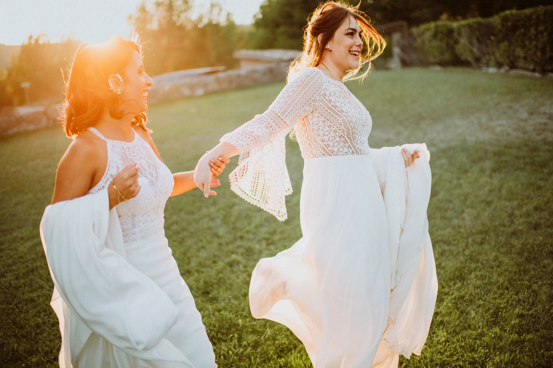 boda LGTBI en Ca n'Alzina (Rubió) — las novias corriendo de la mano por el jardín entre risas a contraluz