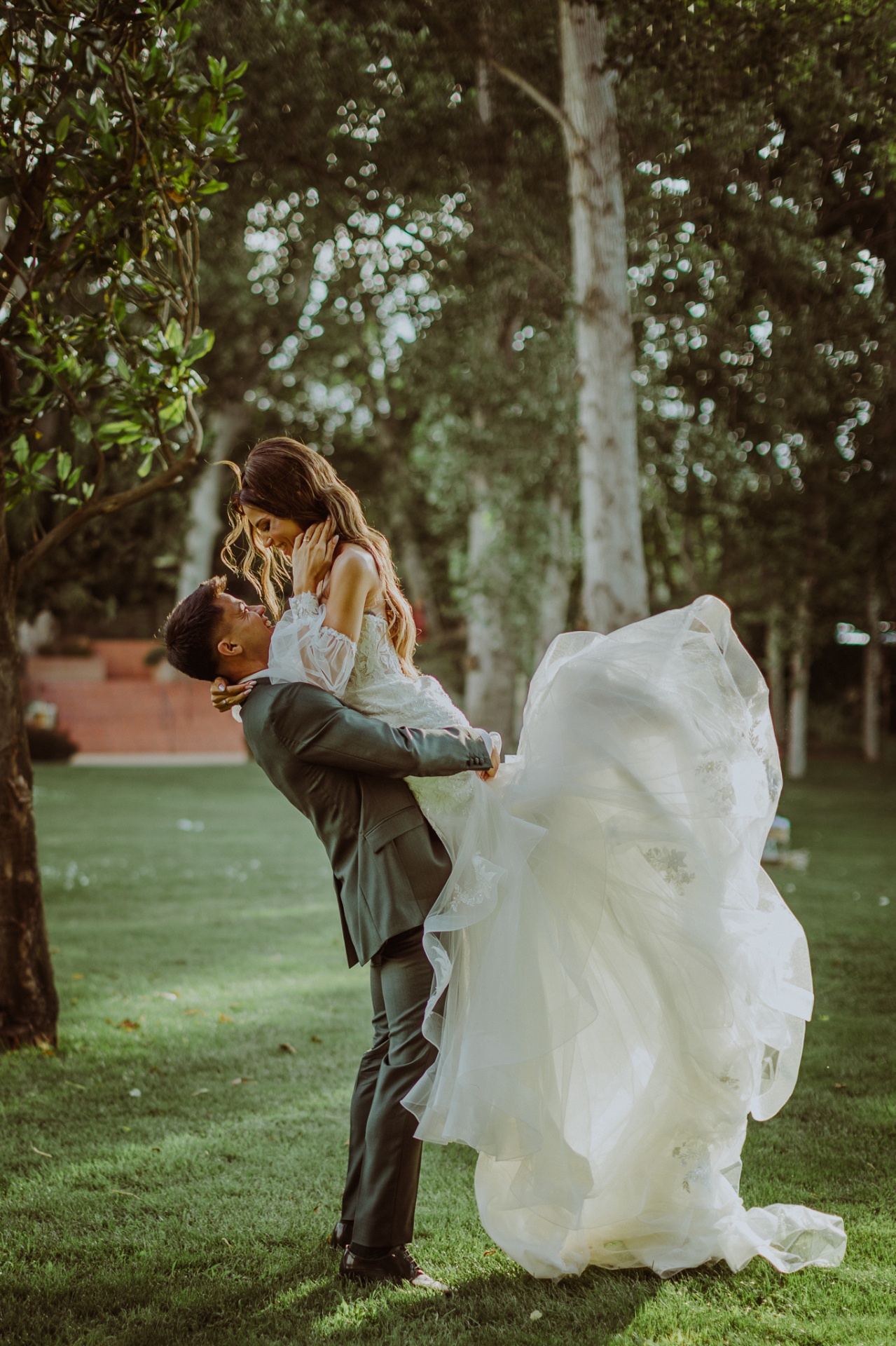 Roger levantando a Alba en brazos besándose con el vestido de tul al viento en los jardines