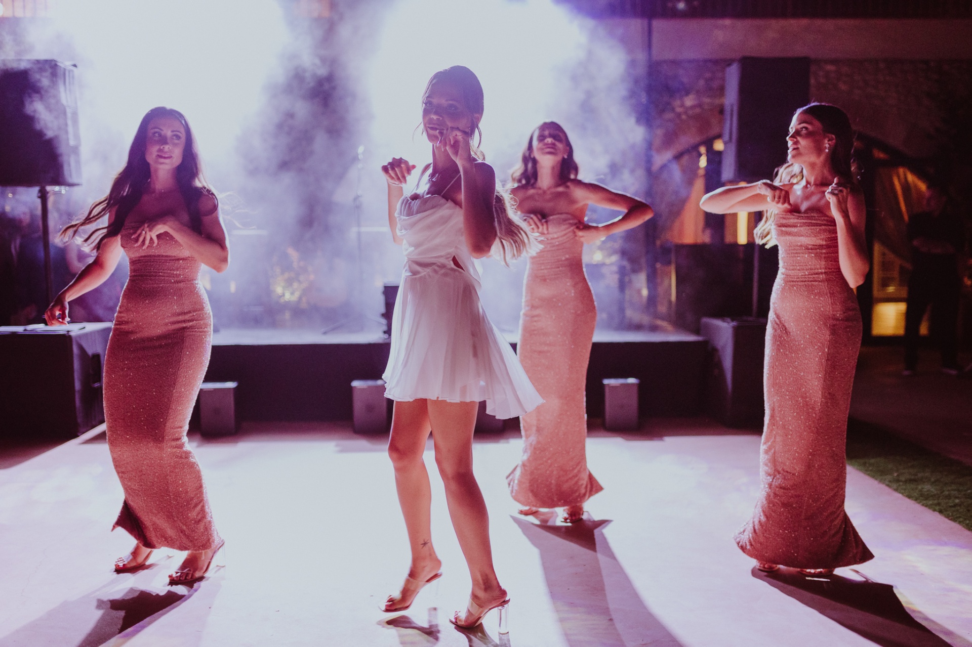 Alba bailando con sus damas de honor con vestido corto blanco en la pista iluminada con humo y luces