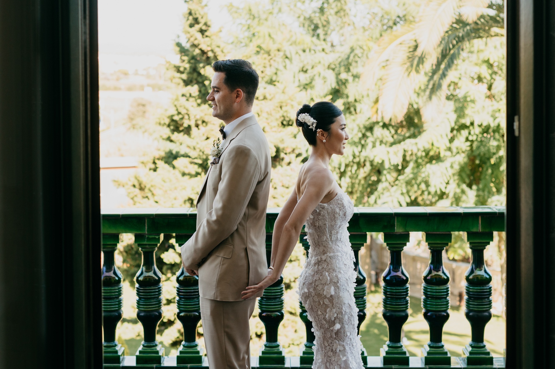 Cameron and Kara standing back to back on the green-tiled balcony of Xalet del Nin during their first look