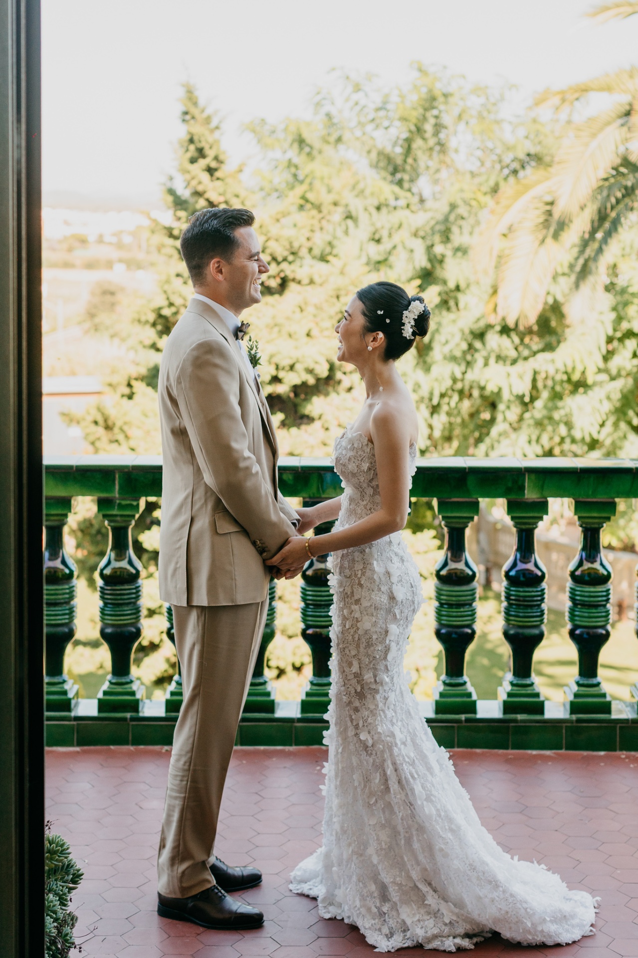 Cameron and Kara holding hands laughing on the balcony of Xalet del Nin with palm trees behind