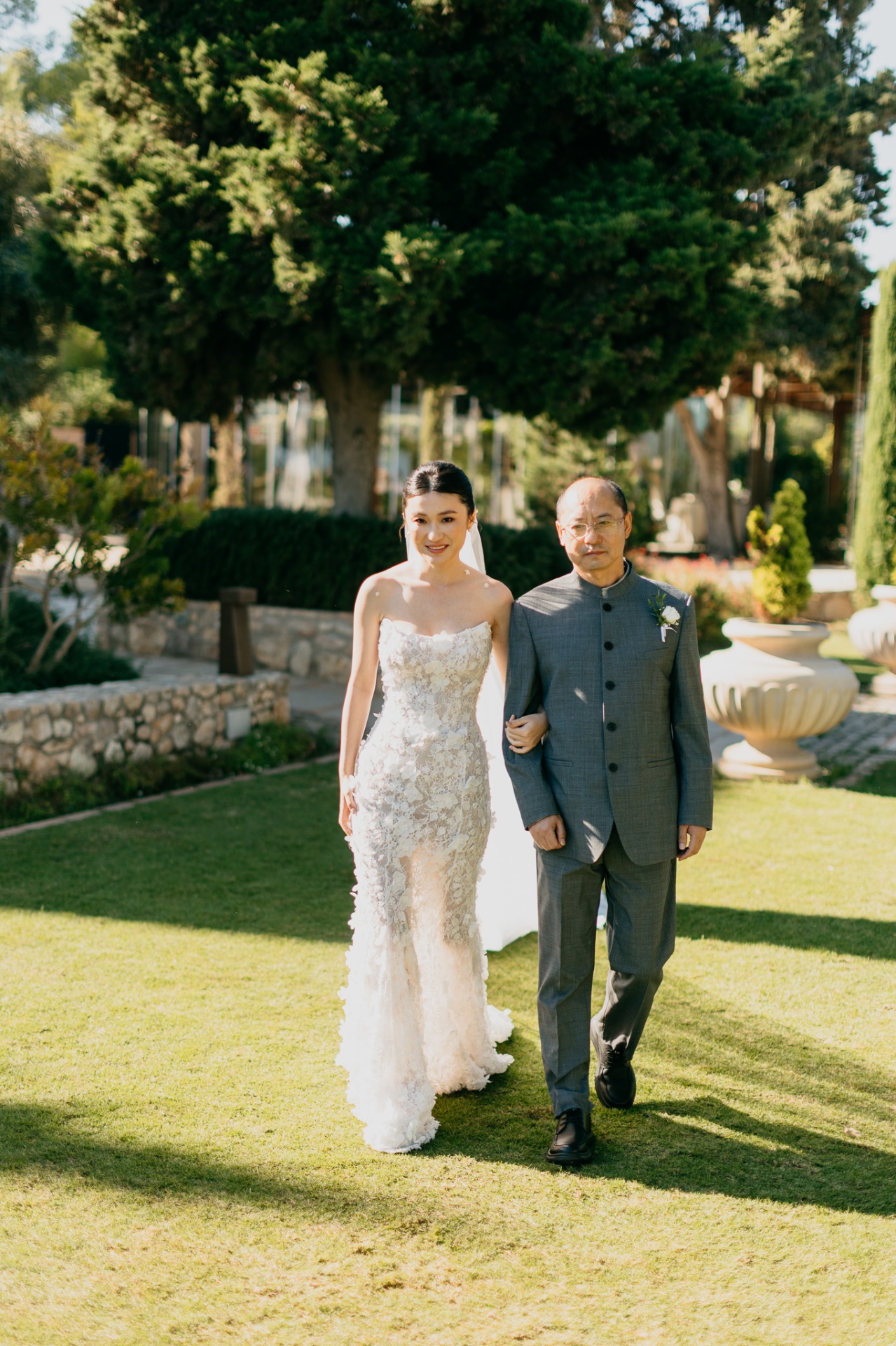 Kara walking down the aisle with her father on the garden lawn at Xalet del Nin