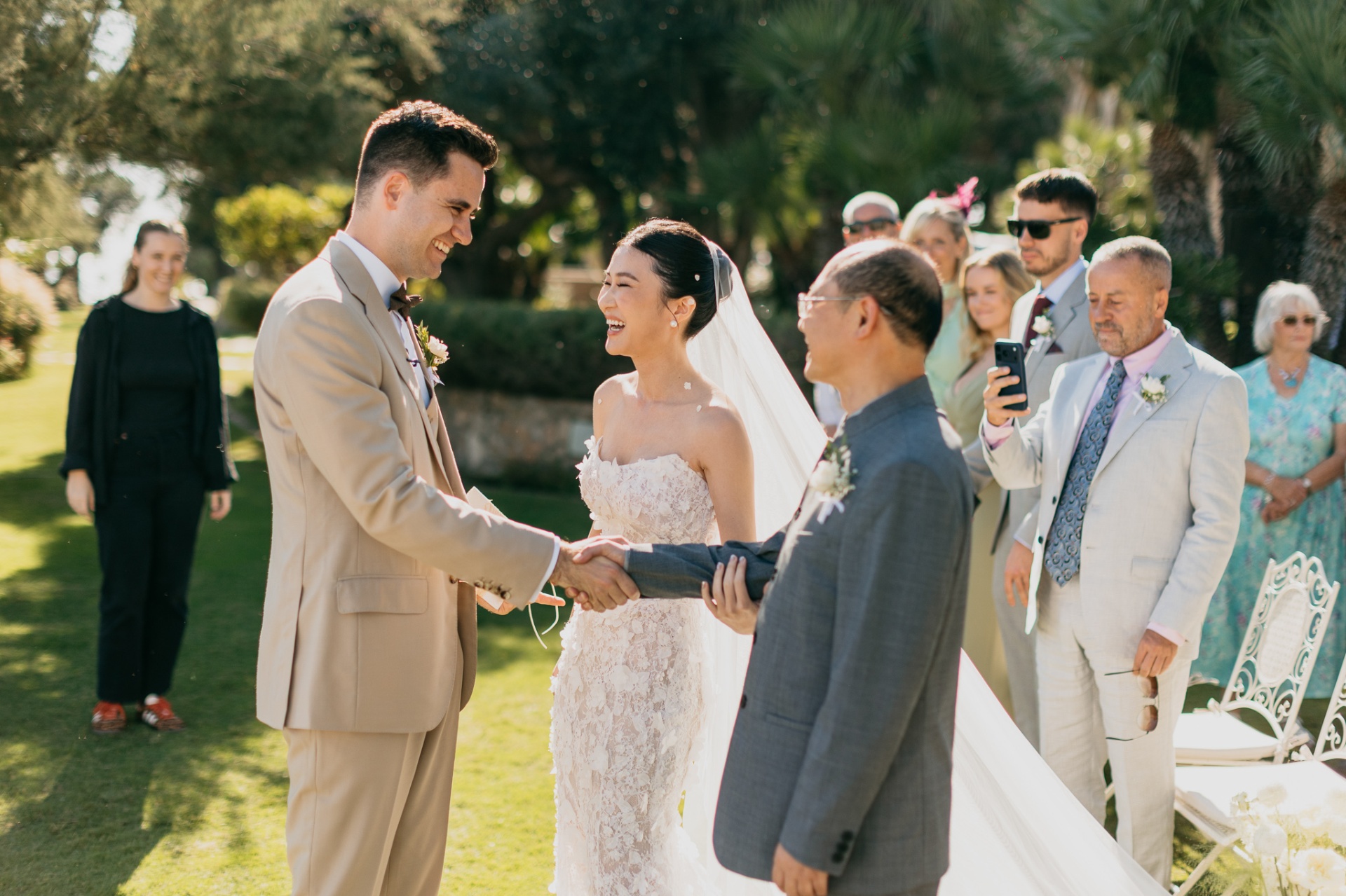 Cameron shaking hands with Kara's father as Kara laughs during the ceremony at Xalet del Nin